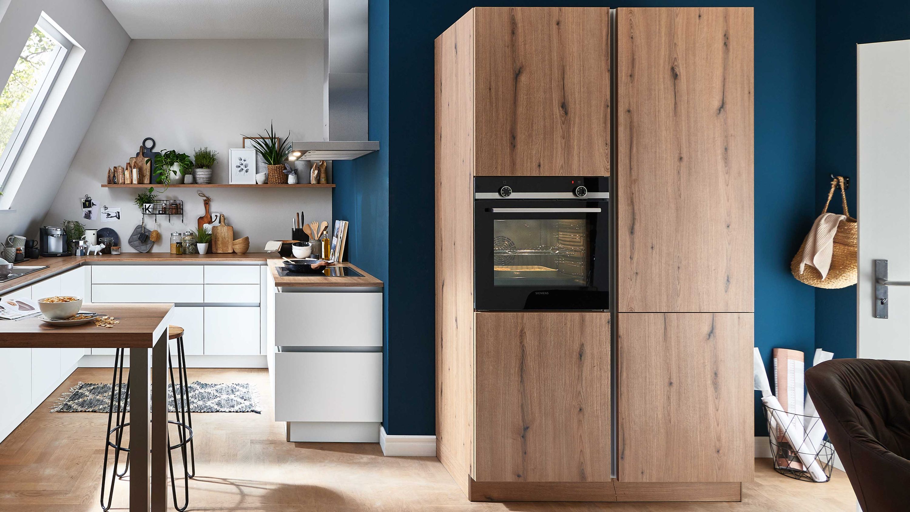 Küche mit blauer Akzentwand und Holzfronten Holzschränke weiße Arbeitsplatte blaue Wand integrierter Ofen Holzboden Tür mit hängenden Taschen