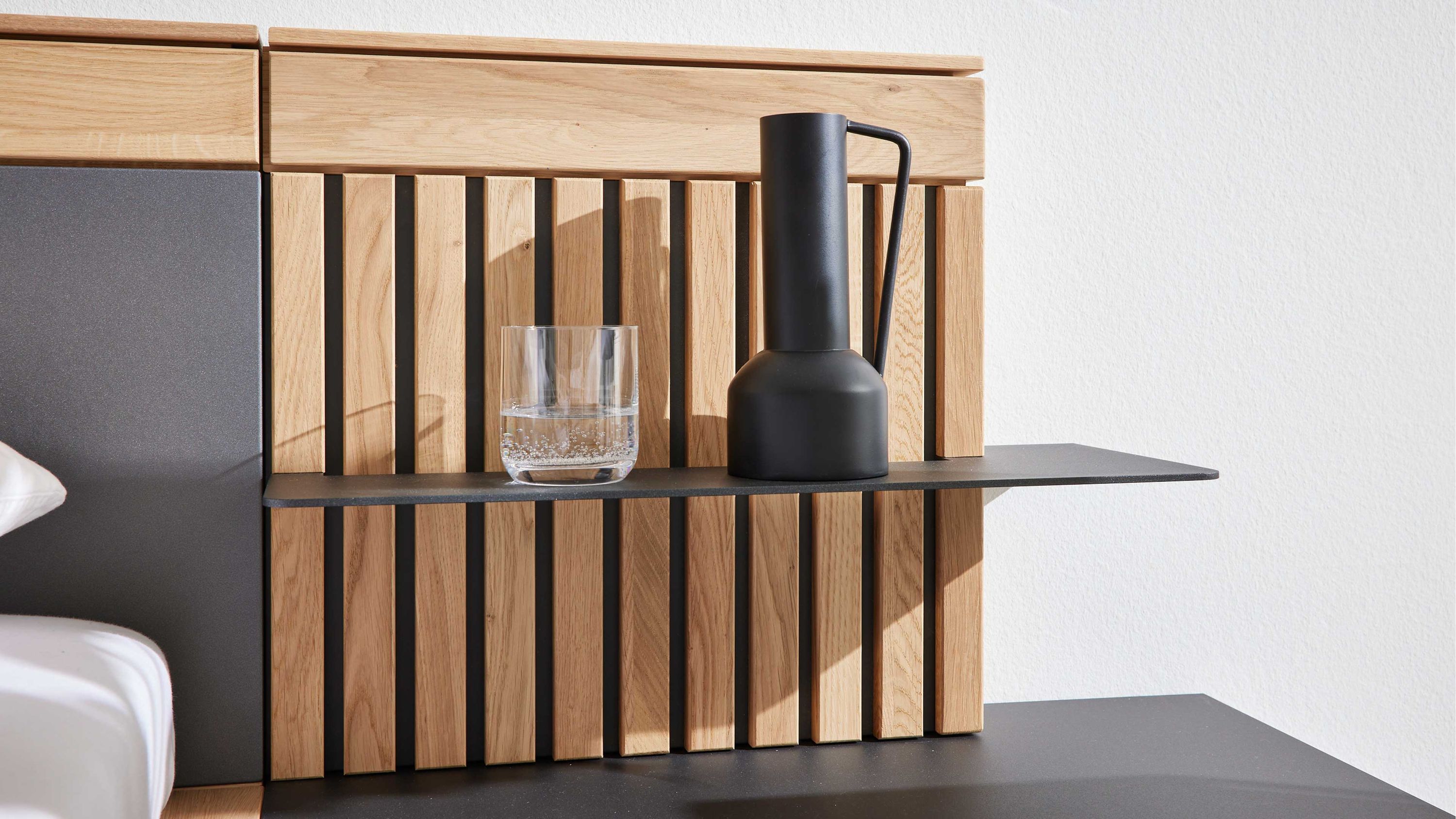 Rechtes Aufsatzpaneel mit senkrechten Holzleisten in heller Farbe und zwei schwarzen Ablageflächen mit Glas und Karaffe