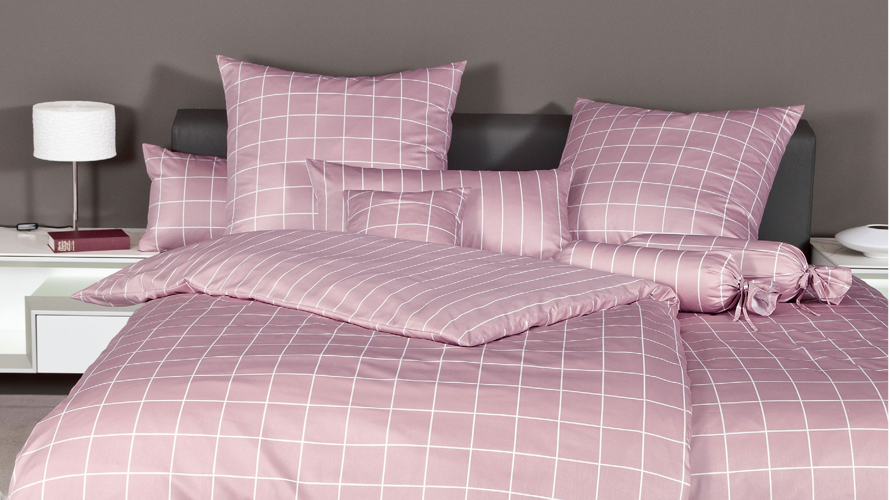 Rosa Bettwäsche mit weißem Karomuster auf Bett mit Kopfteil und mehreren Kissen