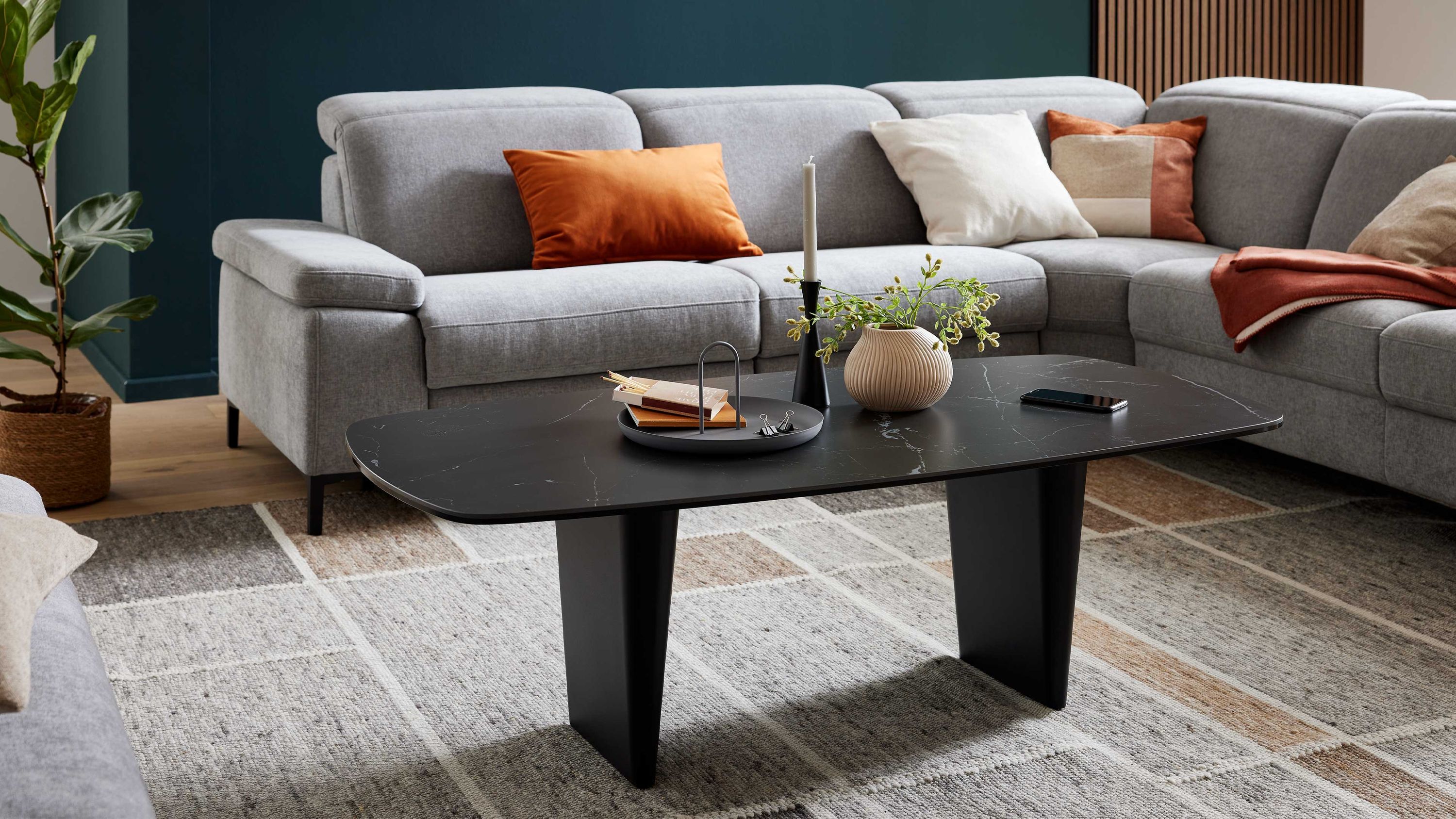 Rechteckiger Couchtisch mit schwarzer Oberfläche und zwei breiten Beinen in einem Wohnzimmer mit grauem Ecksofa