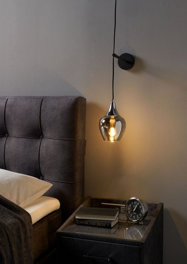 Stilvolles Schlafzimmer mit Details schräge Ansicht eines modernen Schlafzimmers mit Hängelampe, Polsterkopfteil und Nachttisch mit Uhr und Büchern.