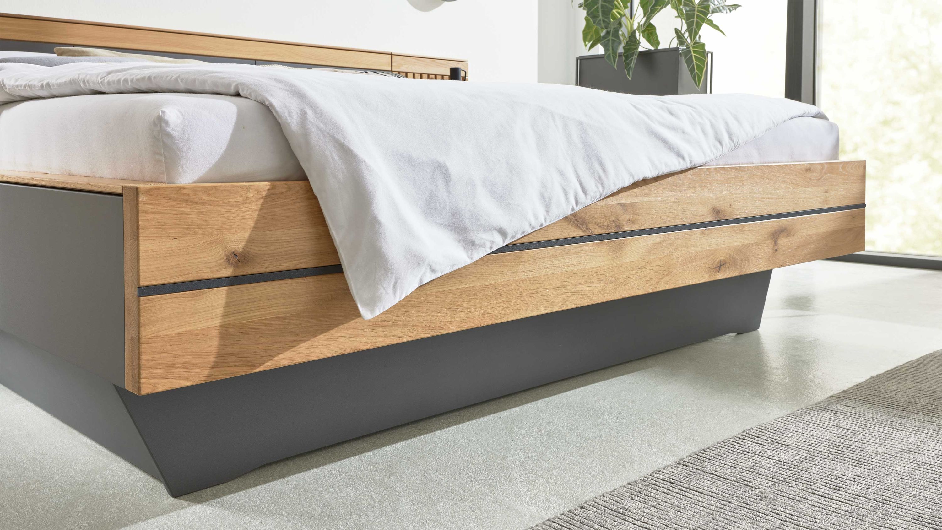 Zweiteiliges Bettschubladen-Set in Holzoptik mit grauer Basis unter einem Bett mit weißer Bettdecke
