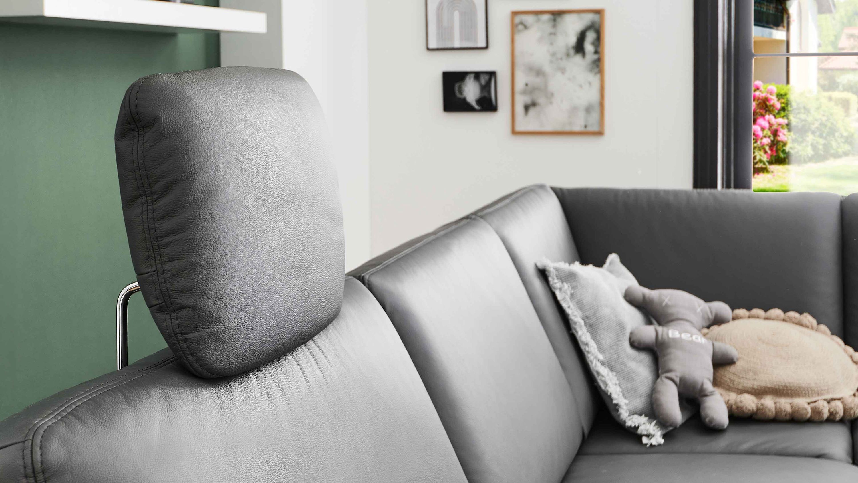 Anthrazitfarbene Kopfstütze aus Leder auf grauem Sofa mit Kissen und Plüschtier