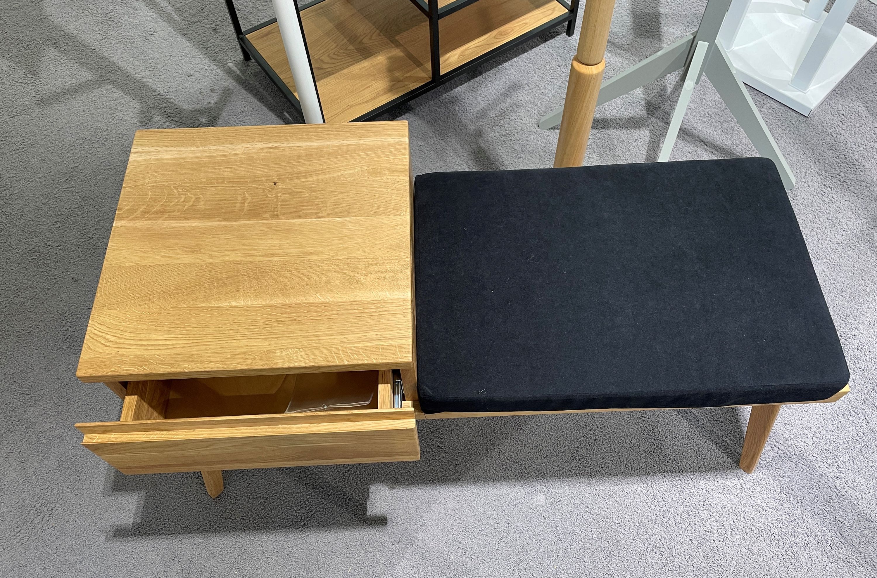 Holzbank mit geöffneter Schublade auf der linken Seite und schwarzem Polster auf der rechten Sitzfläche.