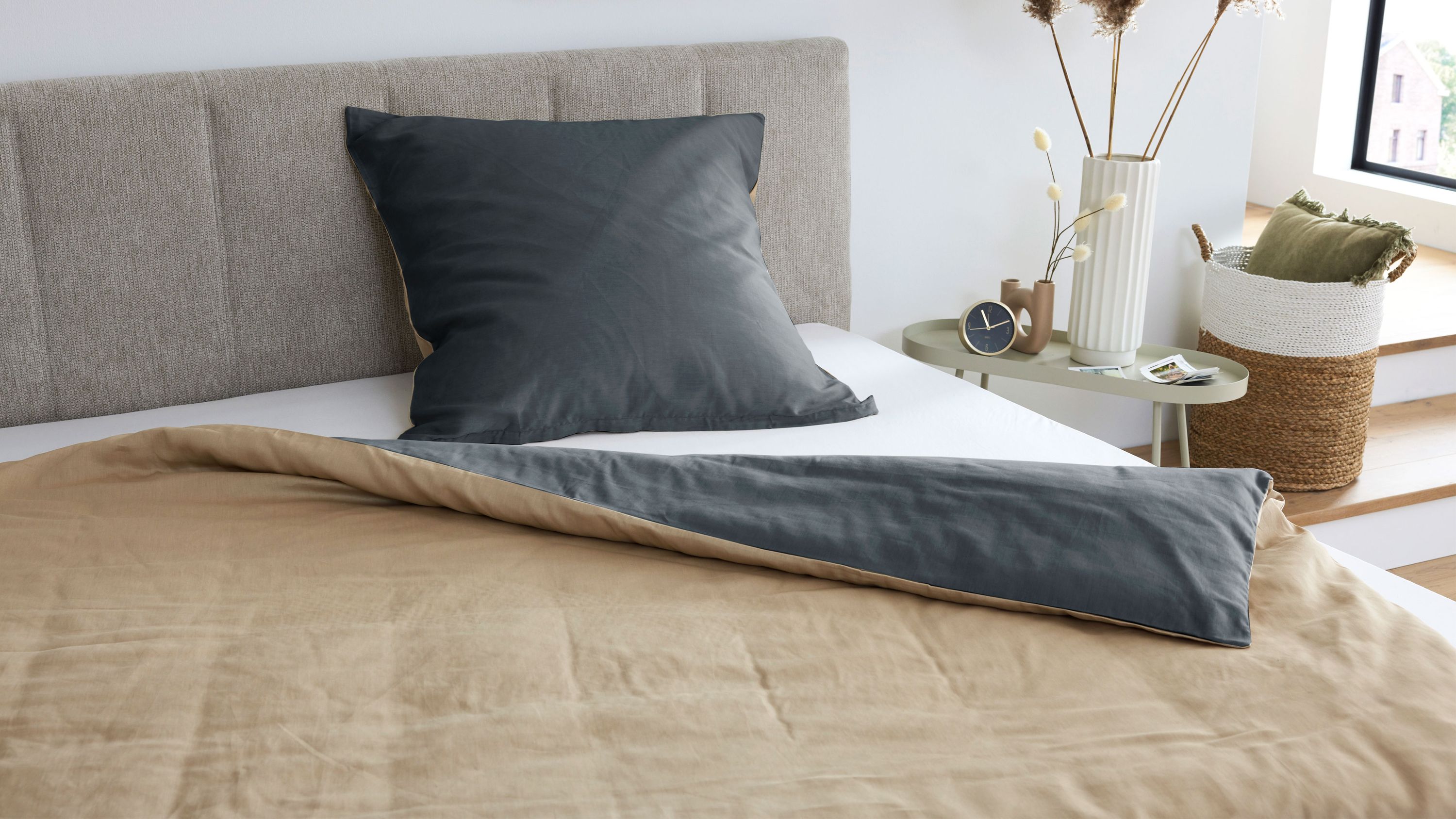 Bett mit hellgrauem Kopfteil Kissen in dunkelgrauer Hülle und Wendebettwäsche in beige und dunkelgrau