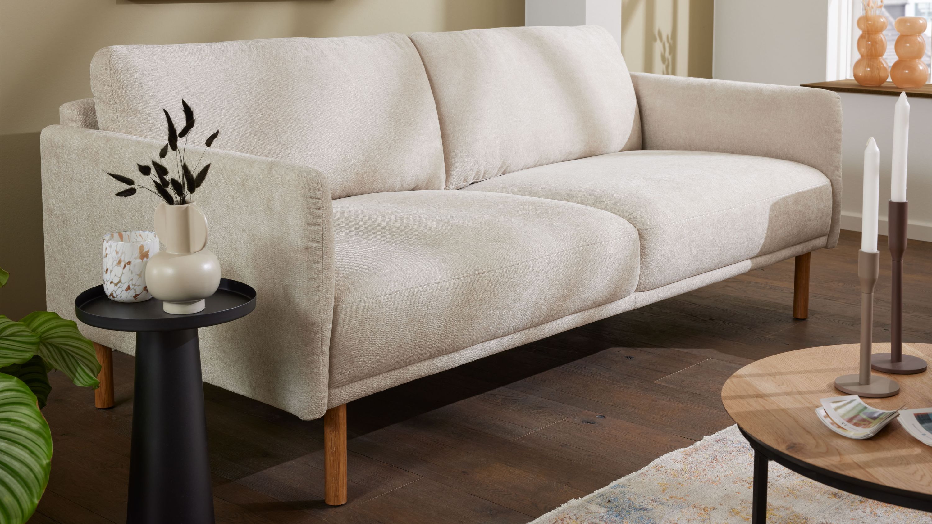 Zweisitziges Sofa mit naturfarbenem Strukturbezug und Holzfüßen in einem Wohnzimmer