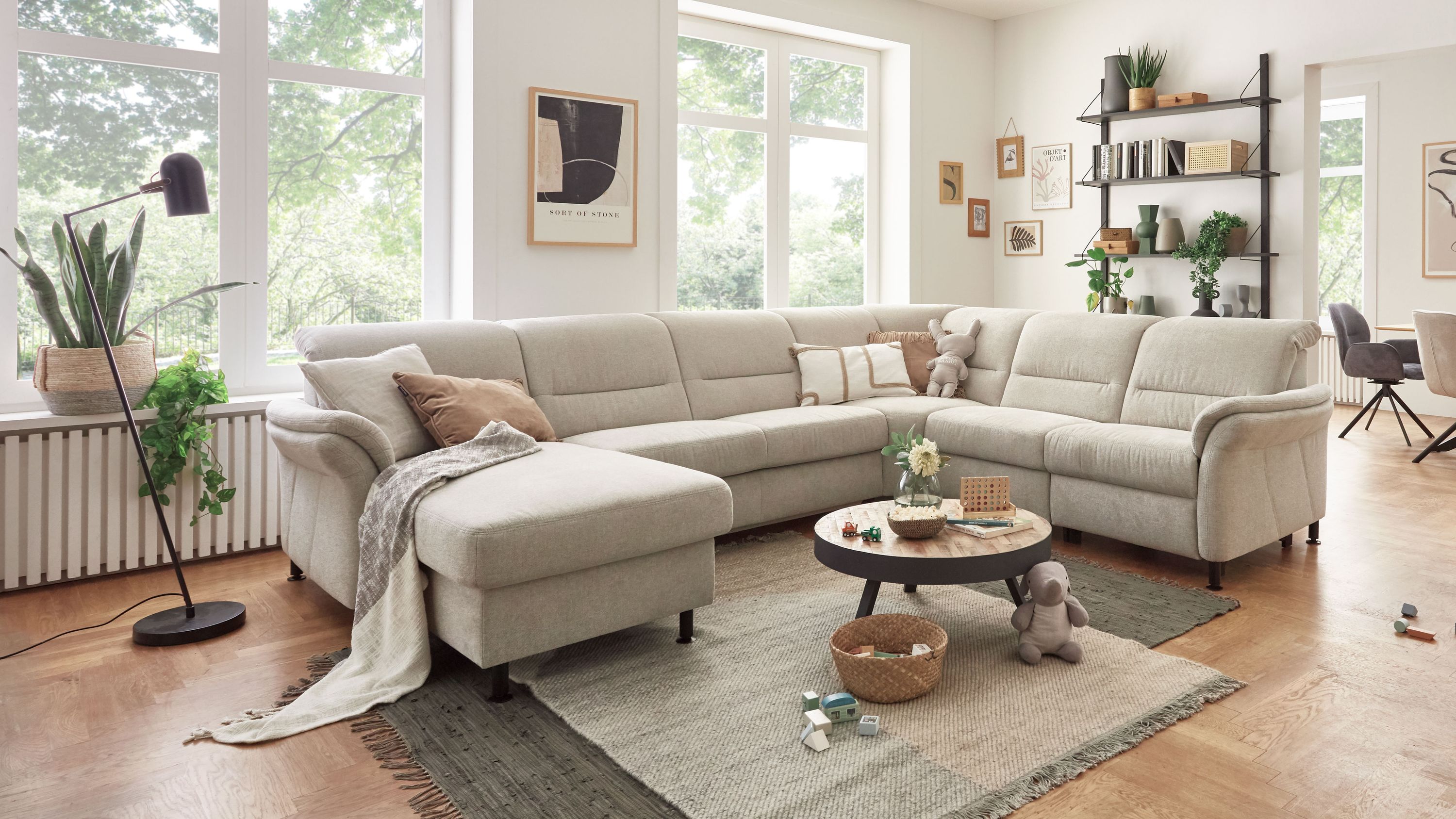 Ecksofa in ecrufarbenem Stoff Ecksofa in ecrufarbenem Stoff mit niedrigen Armlehnen und schwarzen Füßen in hellem Wohnzimmer