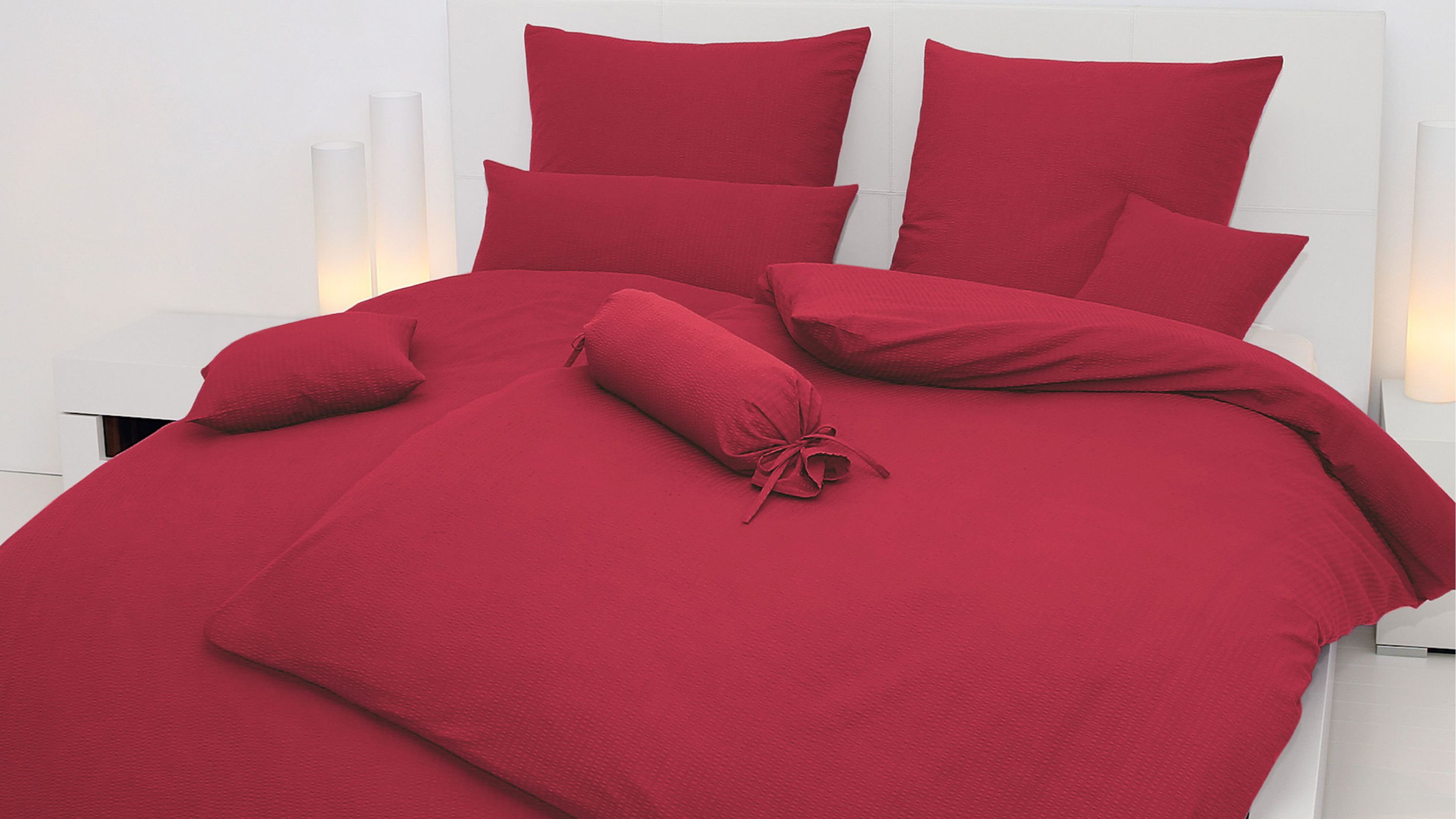 Bett mit burgunderroter Bettwäsche bestehend aus Kissen Decke und Zierkissen