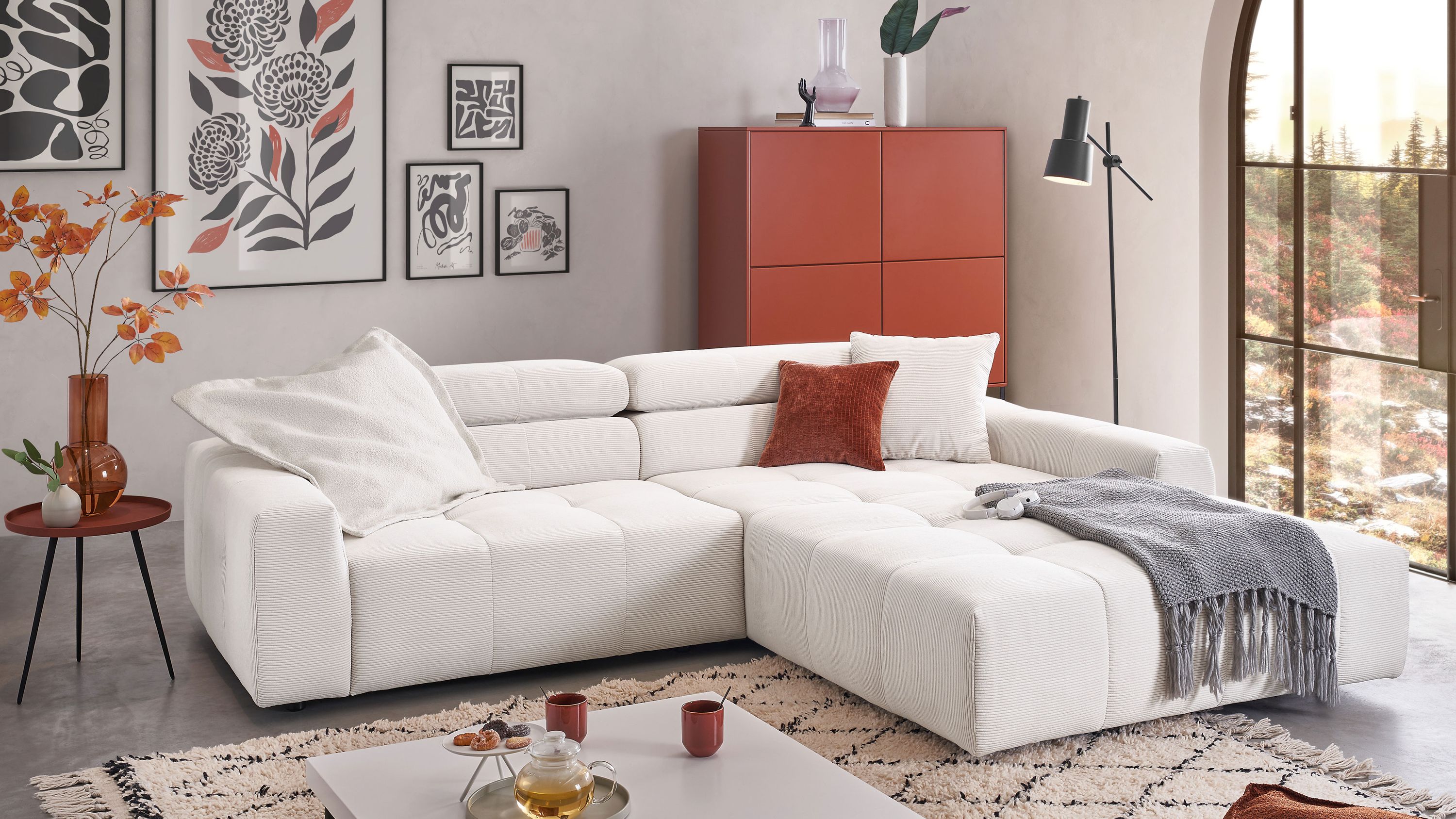Ecksofa mit breiten Armlehnen und Rückenlehnen in weißem Feincord mit Kissen und grauer Decke