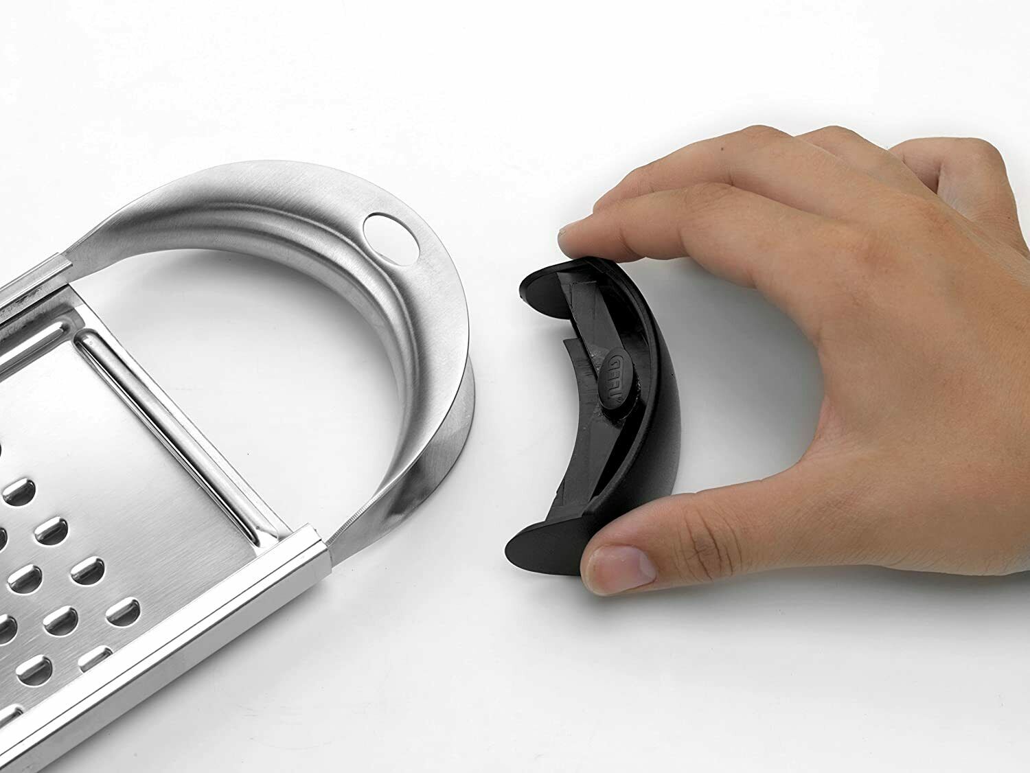 Hand mit Griff neben Metallreibe Hand hält schwarzen Griff neben Metallreibe mit gebogenem Ende, auf weißem Hintergrund fotografiert.