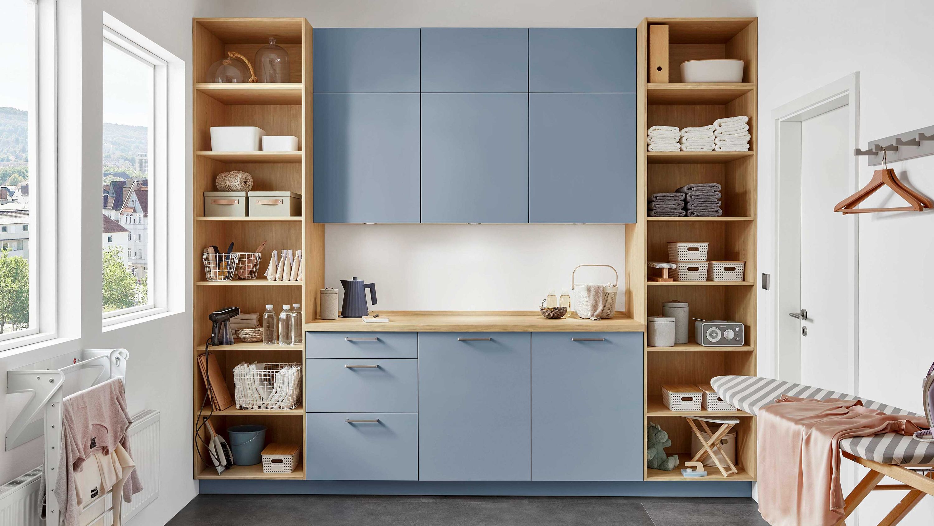 Blaue Schrankküche mit offenen Holzregalen integrierter Spüle heller Rückwand und seitlichen Fenstern.