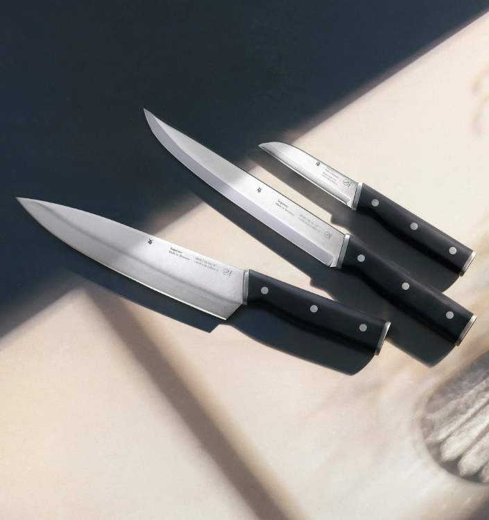 Messer WMF Dreiteiliges Messerset mit schwarzen Griffen und Edelstahlklingen, auf hellem Küchentisch im Sonnenlicht.