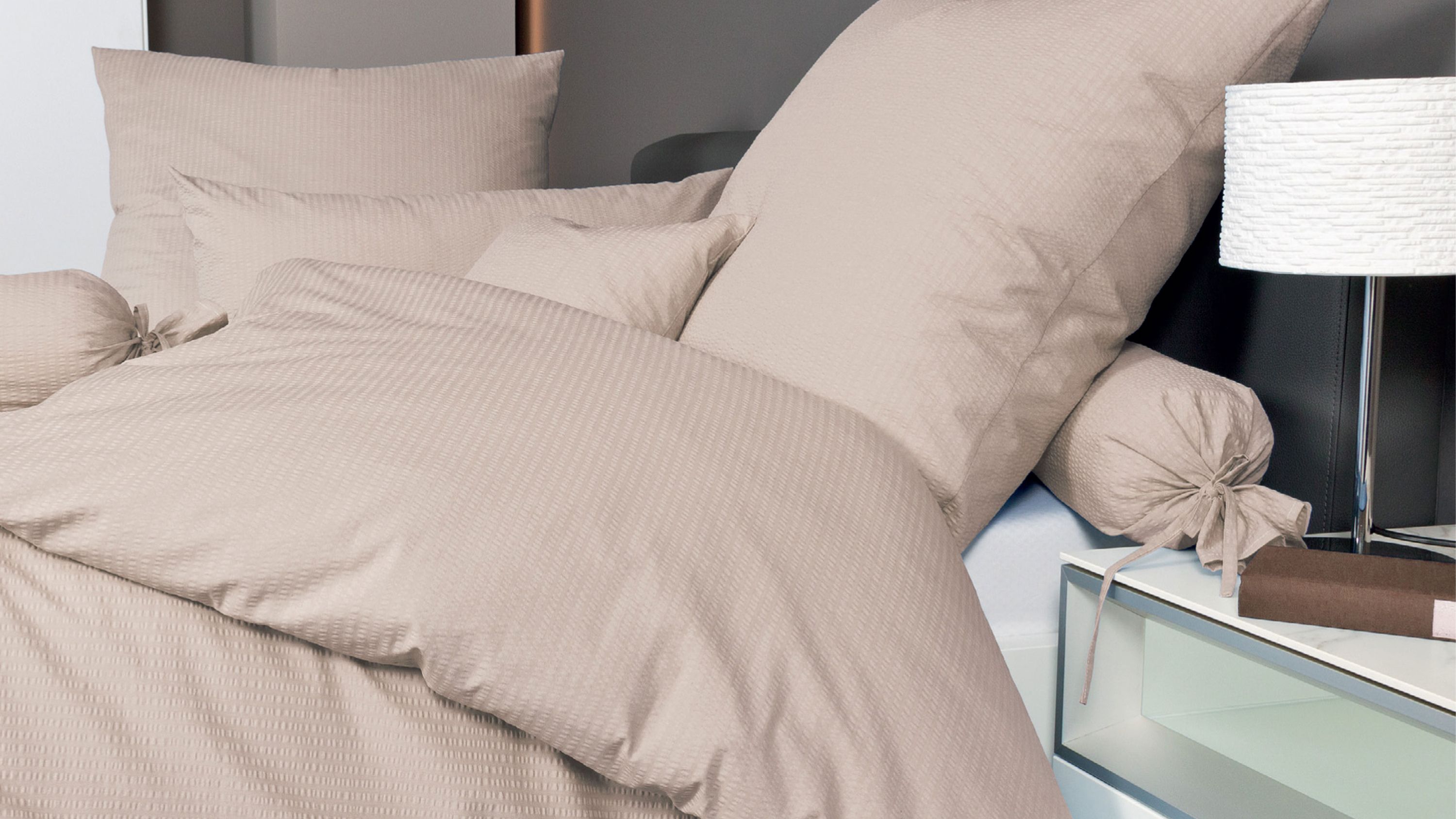 Beige Bettwäsche-Set mit Kissen und Zierkissen auf einem Bett mit schwarzem Kopfteil