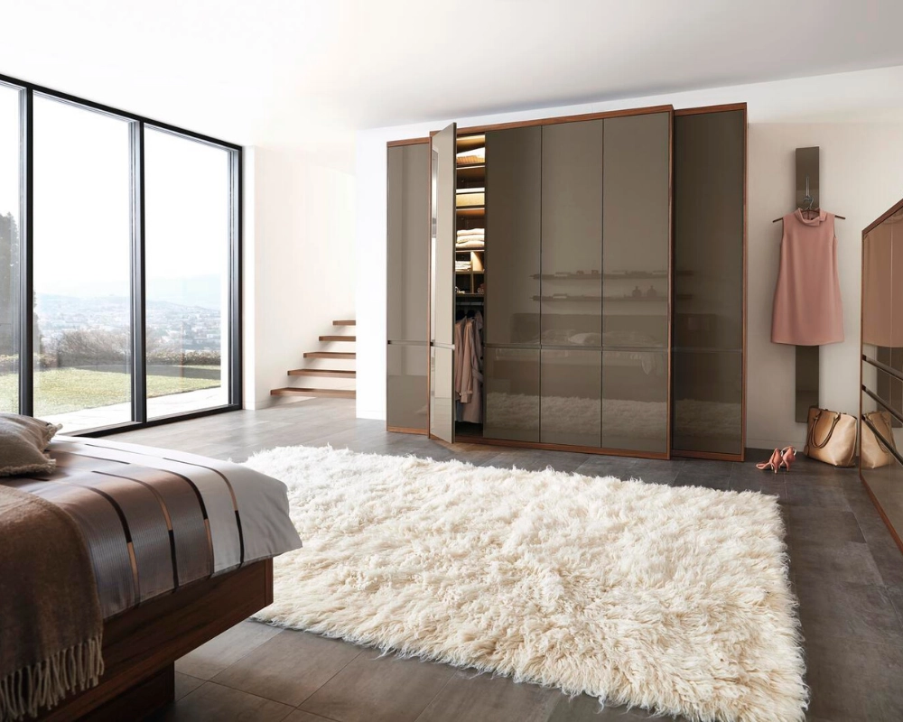 Stilvolles Schlafzimmer mit Designerschrank und gemütlicher Atmosphäre. Modernes Schlafzimmer mit großem Fenster, braunem Bett und glänzendem Schiebetürenschrank in Taupe.