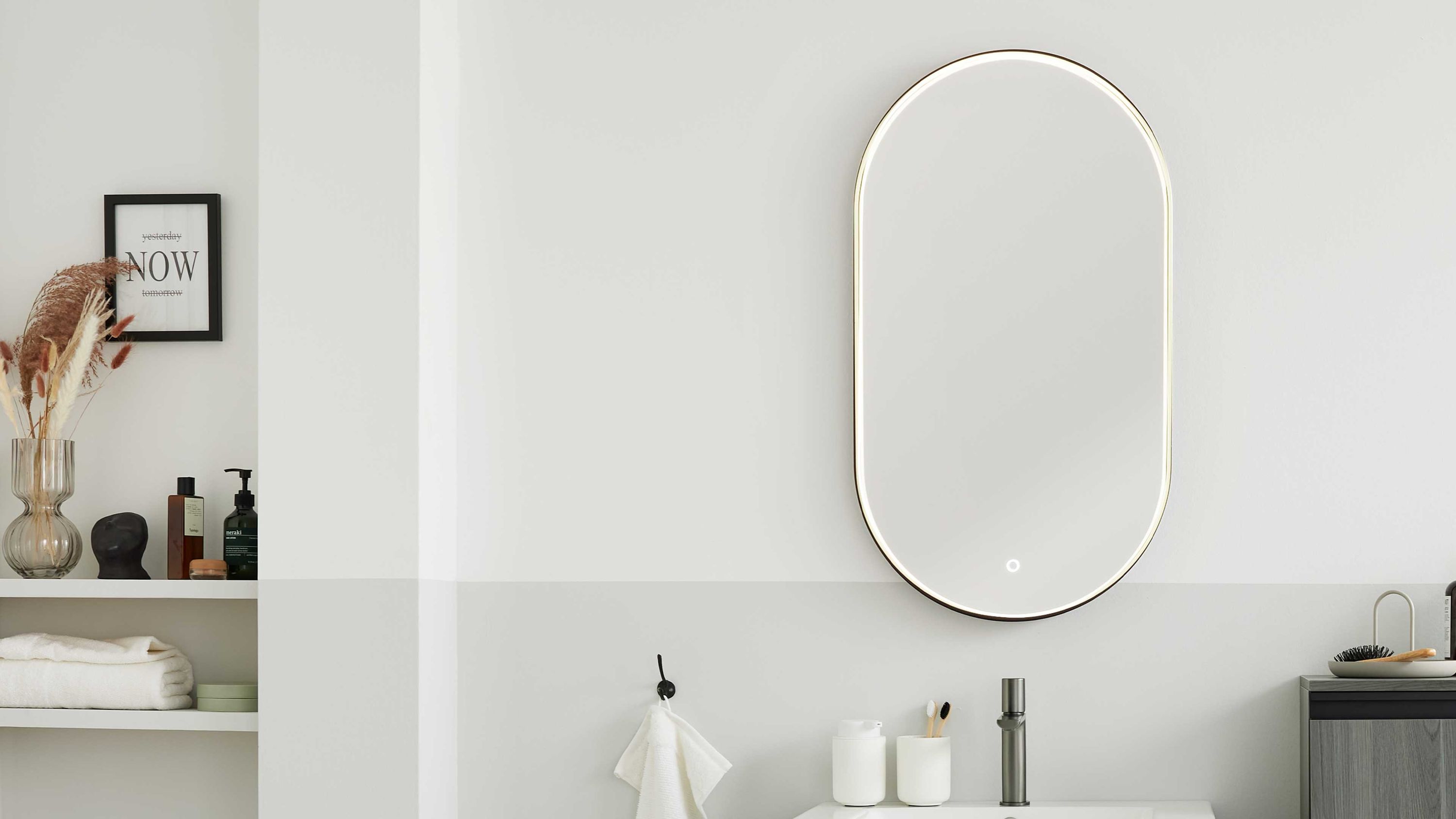 Ovaler beleuchteter Badspiegel an weißer Wand Ovaler Spiegel mit Beleuchtung und Touch-Schalter an weißer Wand über Waschbecken