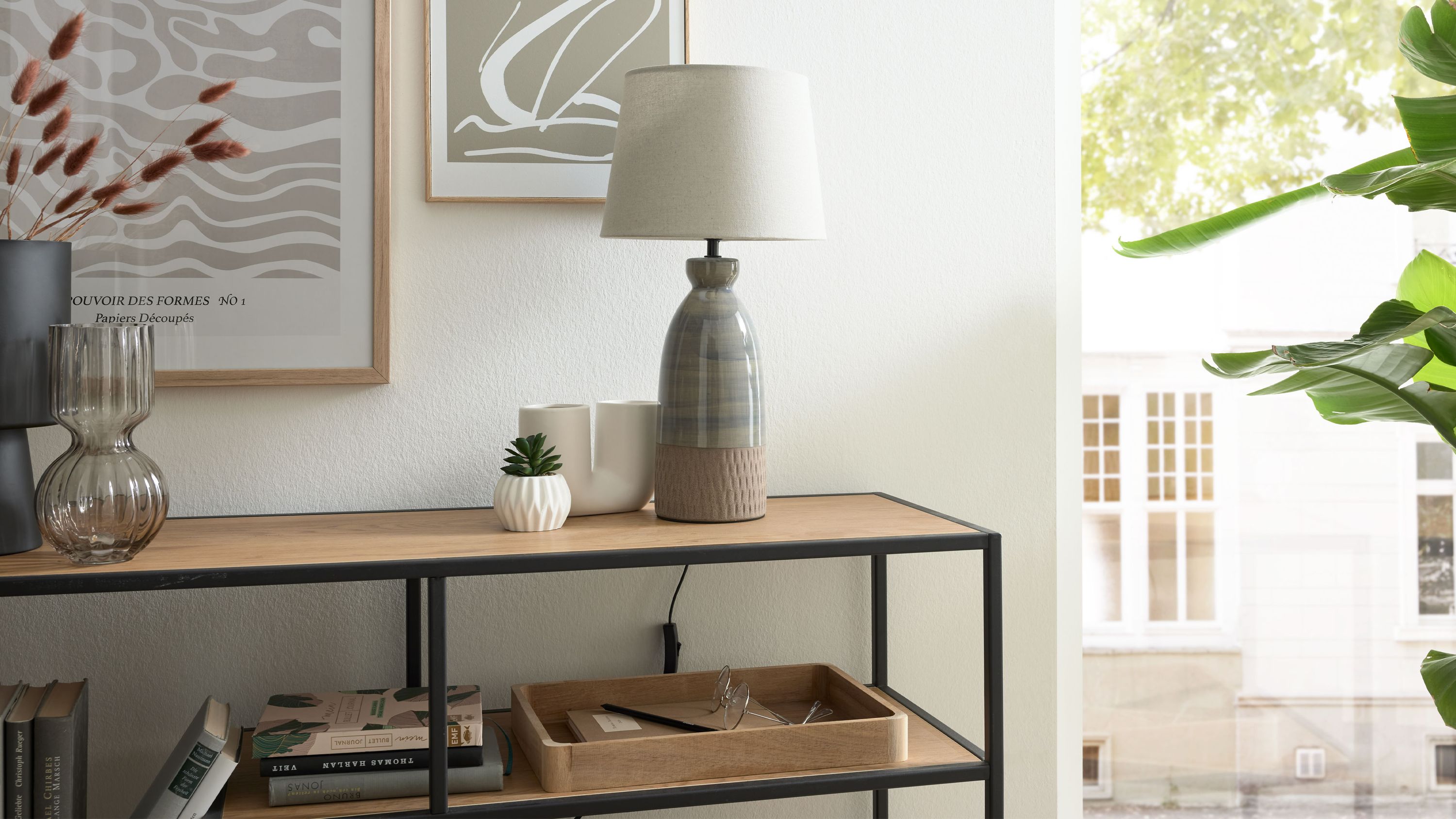 Tischlampe mit grauem Keramikfuß und weißem Lampenschirm auf einem Regal mit Dekoration