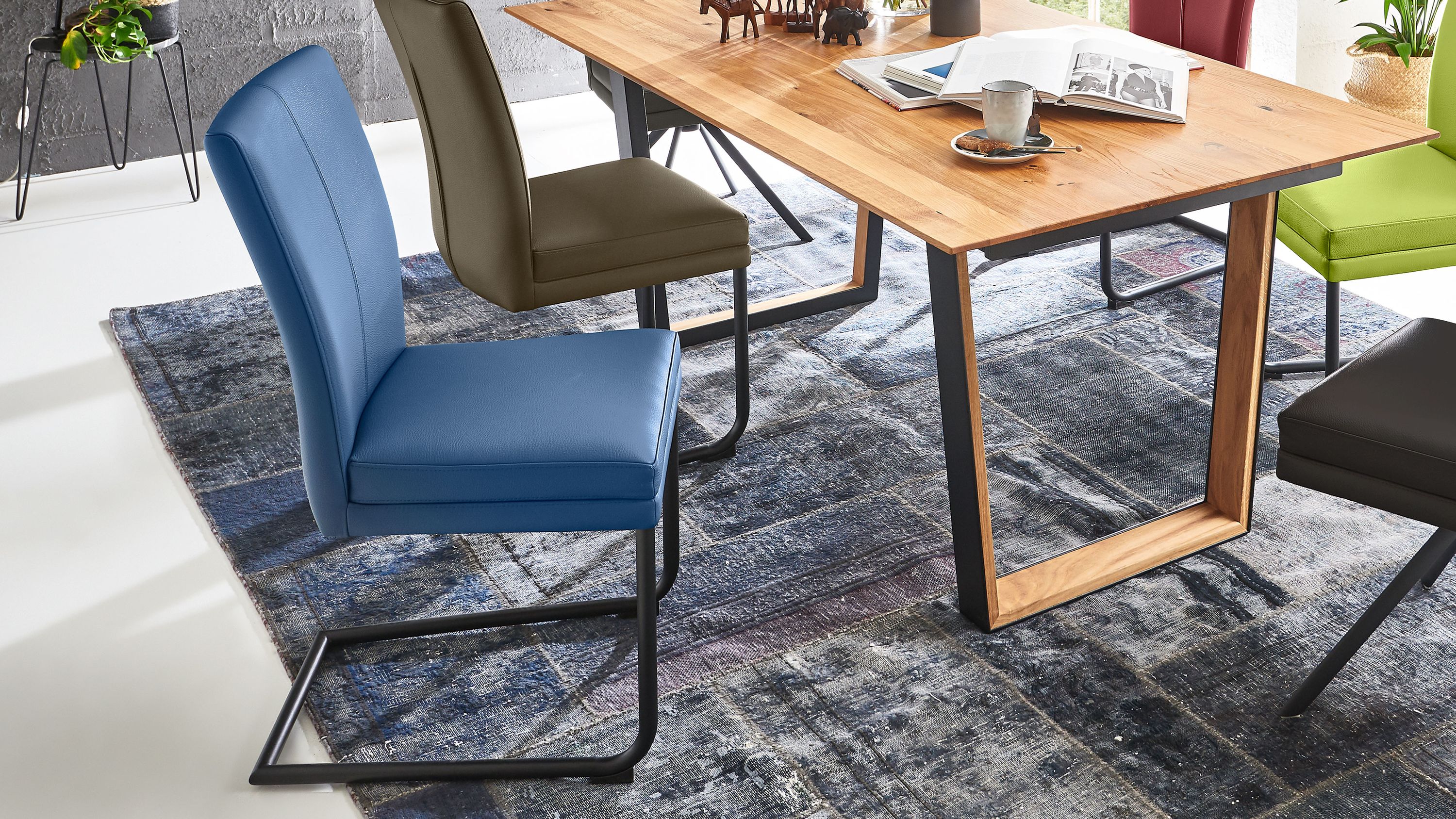 Schwingstuhl mit blauem Sitz und Rückenlehne aus Leder und schwarzem Metallgestell neben einem Holztisch
