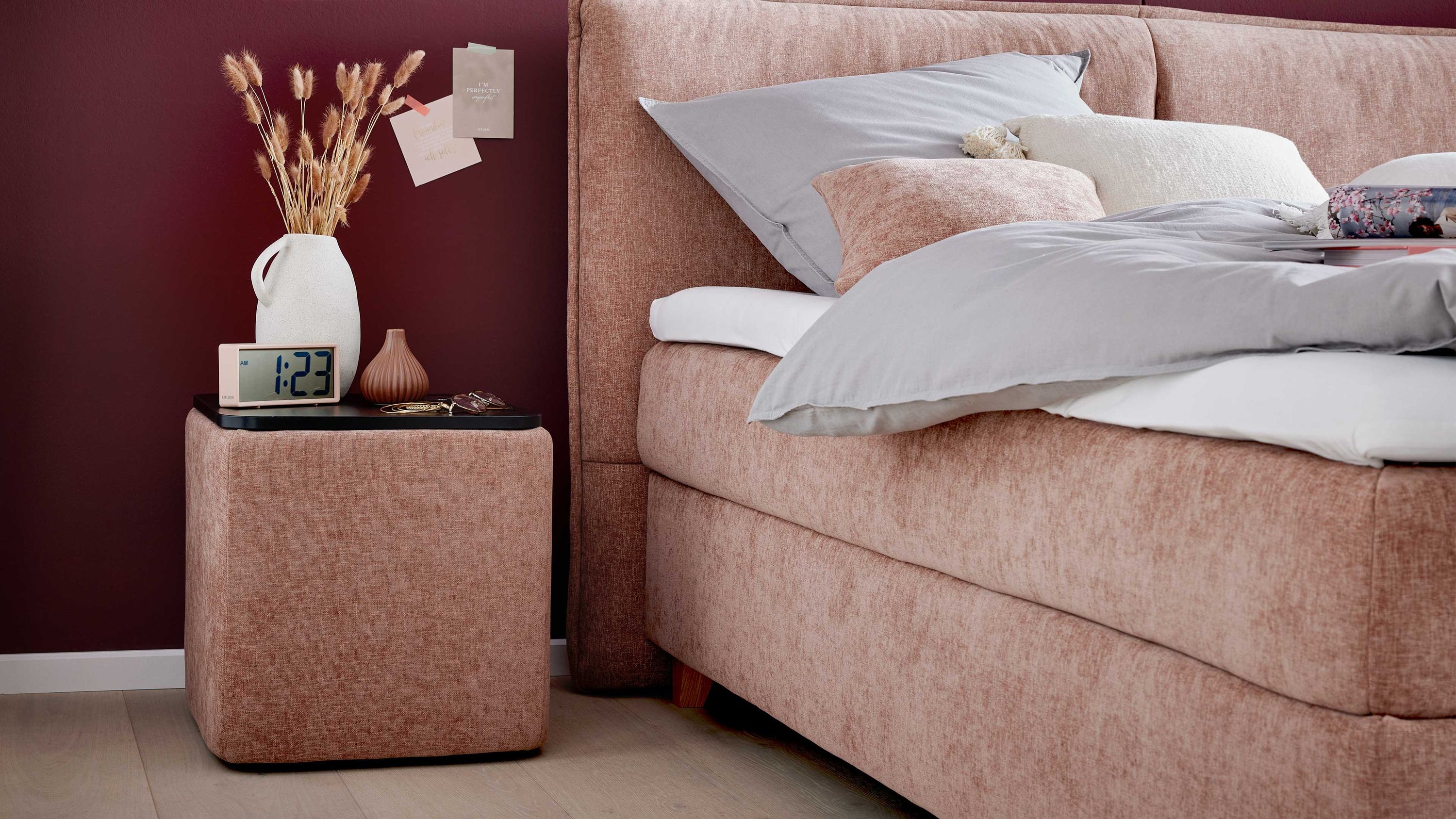 Kubische Nachtkonsole mit sienafarbenem Stoffbezug und schwarzer Ablagefläche neben einem Boxspringbett