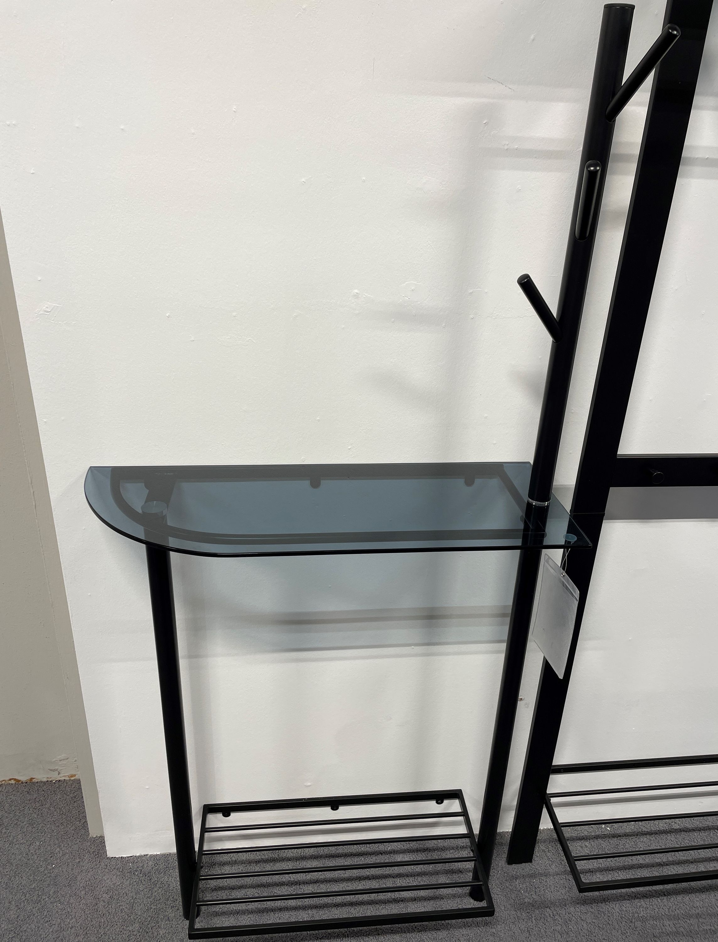 Schlanke Glasablage mit halbrunder Platte, schwarzem Metallgestell und unterem Ablagerost.