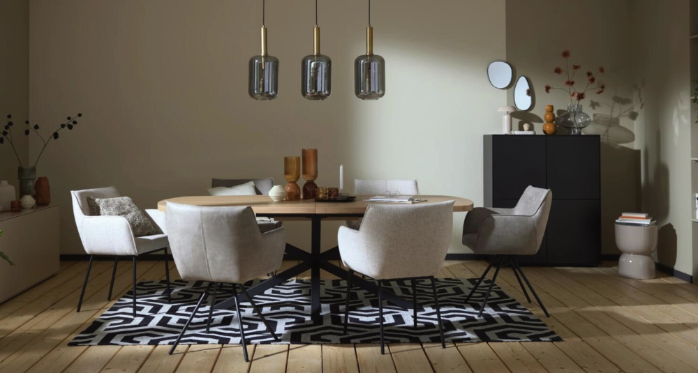 Esszimmer mit rundem Holztisch, weißen Polsterstühlen, schwarzem Teppich mit Muster und modernen Pendelleuchten.