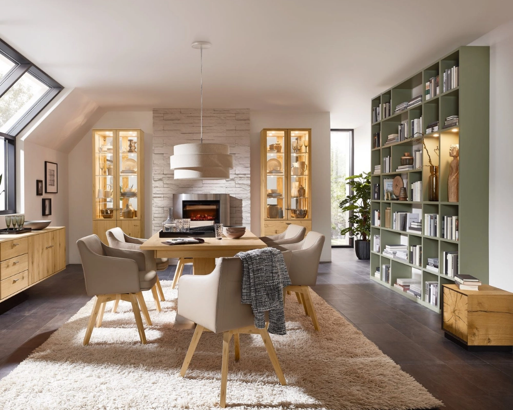 Stilvolles Esszimmer im Landhausstil mit rundem Esstisch, Kamin und wohnlicher Vitrinenwand. Esszimmer mit runder Holztischgruppe, Kamin, Hängeleuchte und Vitrine in modernem Landhausstil mit Naturtönen
