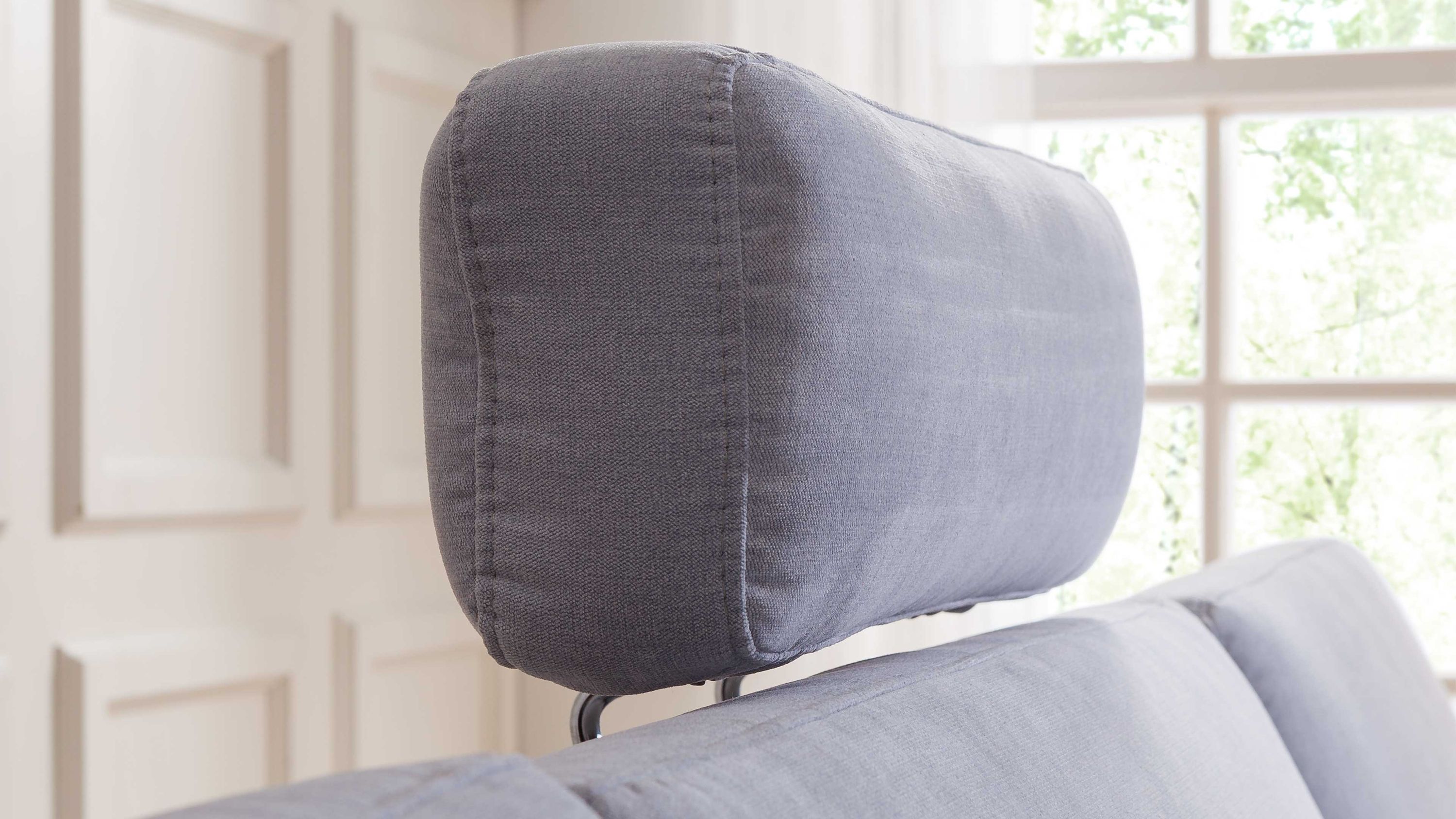 Kopfstütze in hellblau auf Sofa Hellblaue gepolsterte Kopfstütze mit abgerundeten Ecken auf einem Sofa vor Fenster