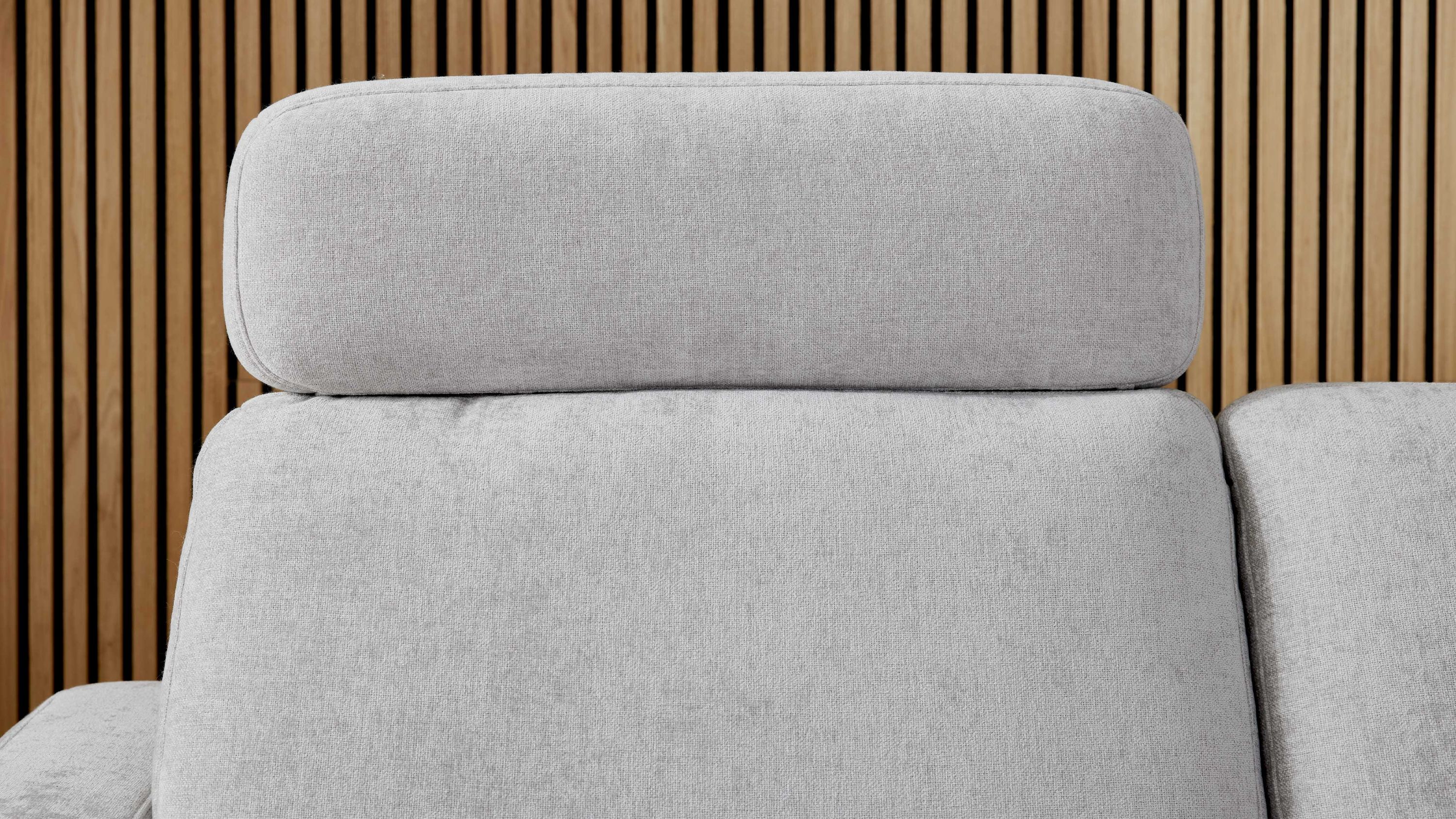 Schlafsofa mit silberfarbener Kopfstütze aus Chenille und hellgrauem Bezug vor Holzlamellenwand