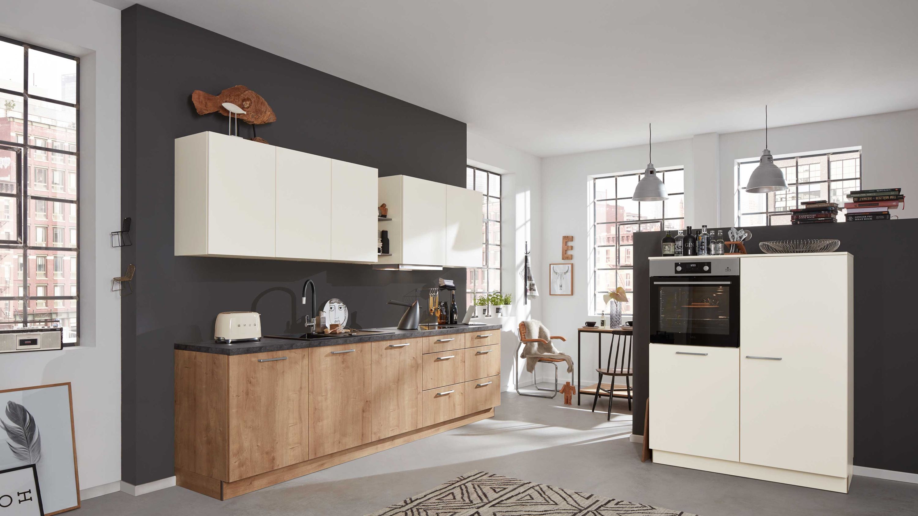 Moderne Küche mit Materialmix Lichtakzenten und integriertem Essbereich Küche mit Holz-weiß-Fronten schwarzer Arbeitsplatte Hängelampen Fensterlicht Einbaugeräte rechts Essbereich hinten