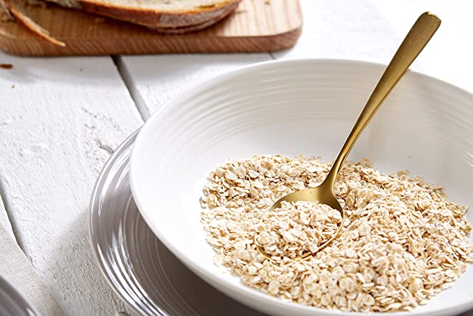 16-teiliges Geschirrset in Grau-Weiß mit Müslischale Schale in Weiß mit Müsli und goldfarbenem Löffel  Brotscheiben auf Holzbrett im Hintergrund