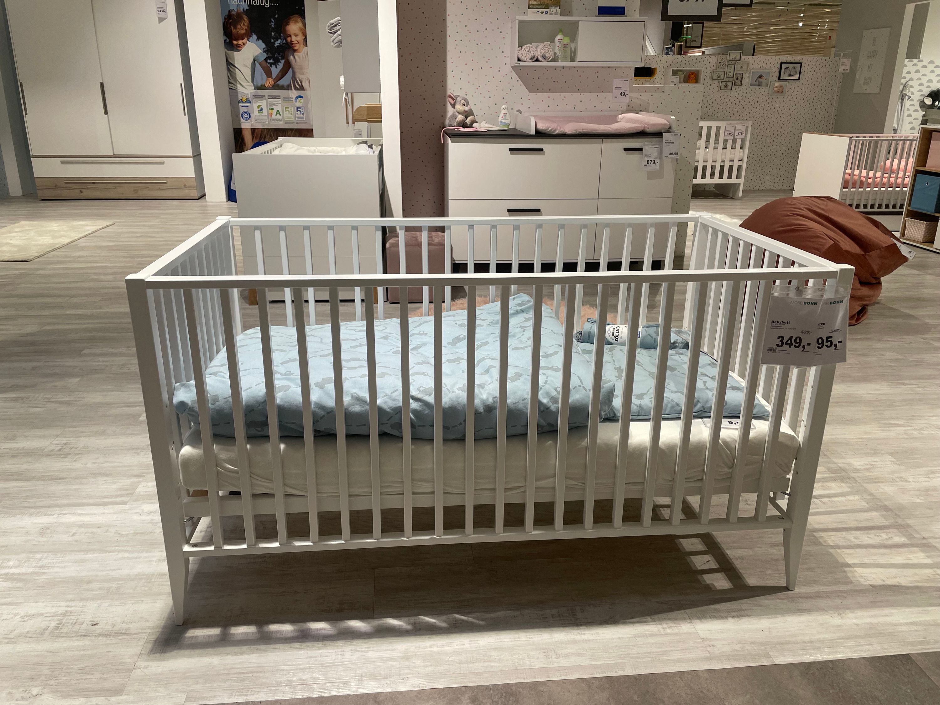 Weißes Babybett mit Gitterstäben und blauer Matratze in einem Möbelgeschäft