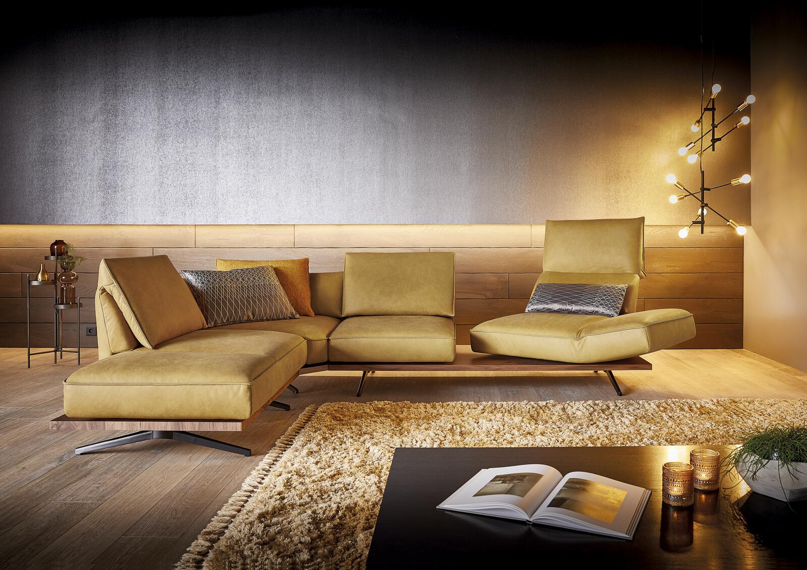 Designsofa von Koinor in senfgelbem Leder mit modularen Sitzelementen und Holzdetails, dekoriert mit Kissen, in modernem Wohnzimmer mit stimmungsvoller Beleuchtung.