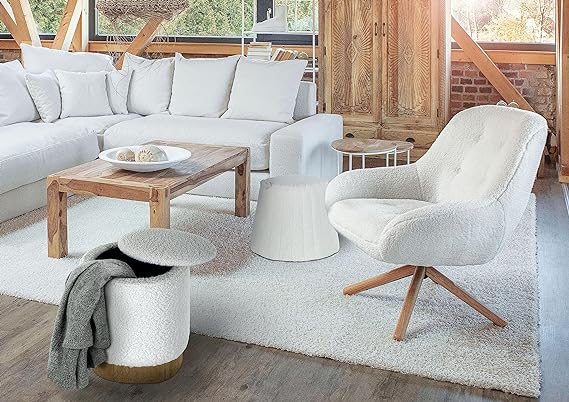 Weißer Polsterhocker mit grauer Decke leicht schräg aufgenommen im modernen Wohnzimmer mit Sofa Tisch und Fenstern