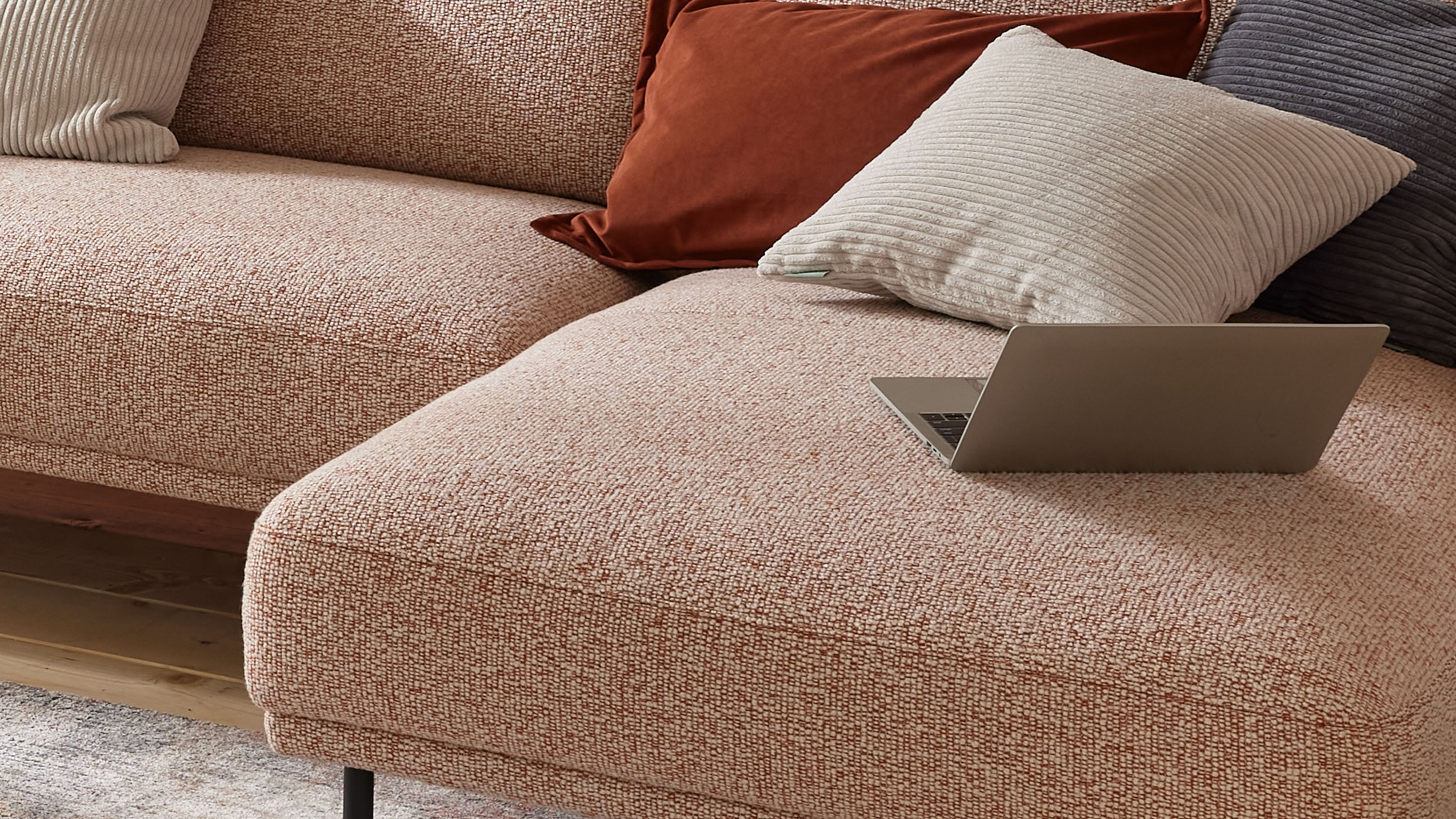 Beige Kissenhülle mit breiten Cordstreifen auf einem hellen Sofa neben einem Laptop