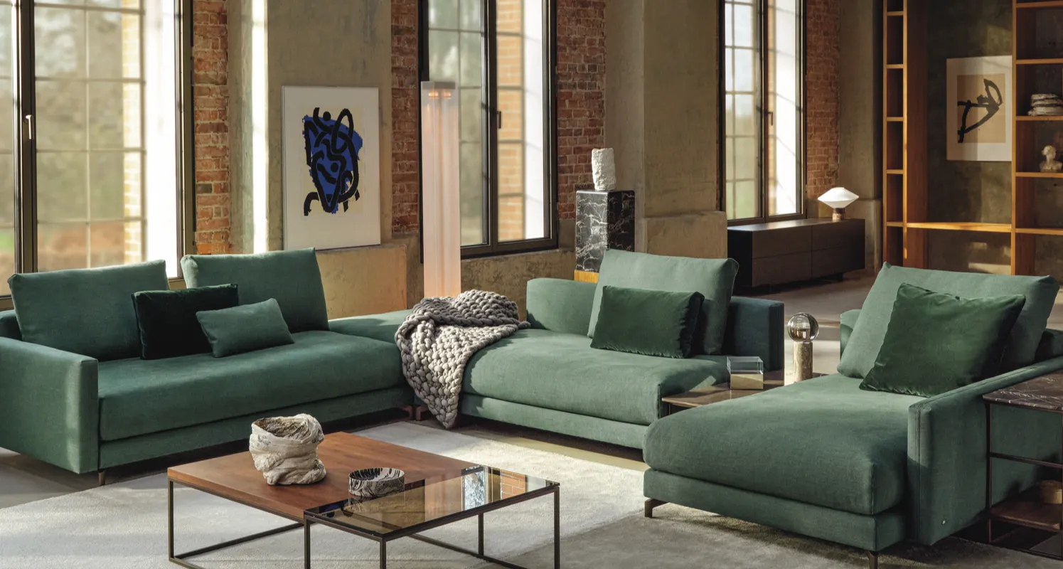 Moderne beige Ecksofa-Landschaft mit verstellbaren Rückenlehnen und Zierkissen, platziert in einem hellen Wohnzimmer mit Naturstein-Tisch und dekorativen Kakteen.