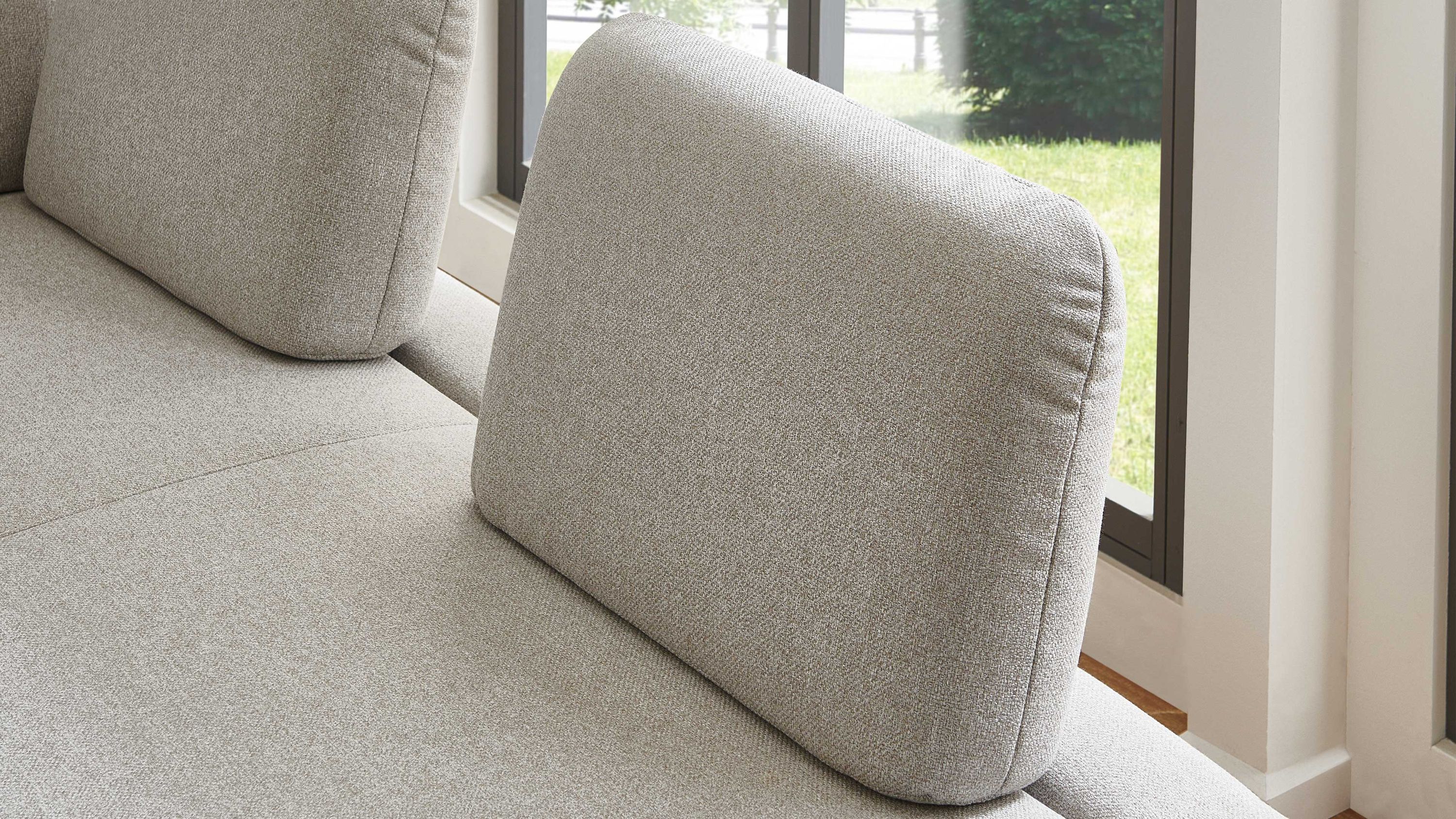 Sitzfläche mit zwei rechteckigen silberfarbenen Polsterkissen auf einem Sofa vor Fenster