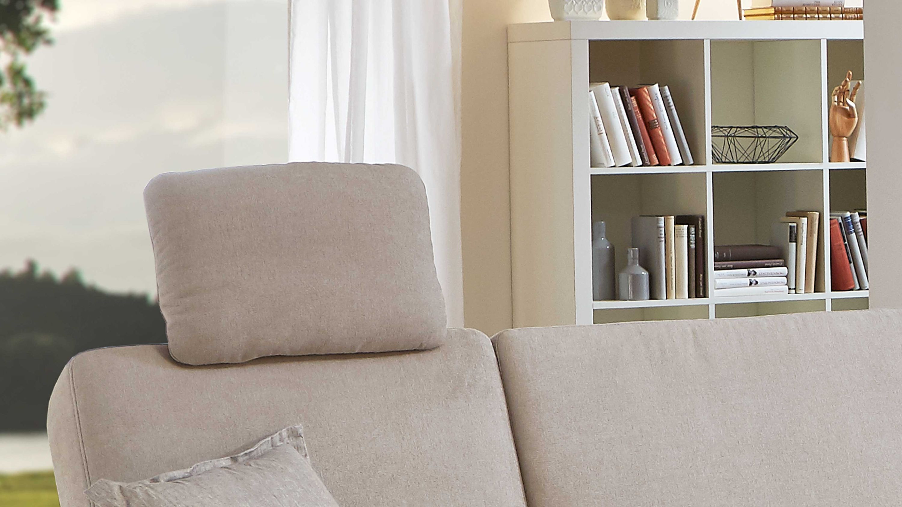 Ecrufarbene Kopfstütze aus Mikrofaser auf einem Sofa vor einem weißen Regal mit Büchern