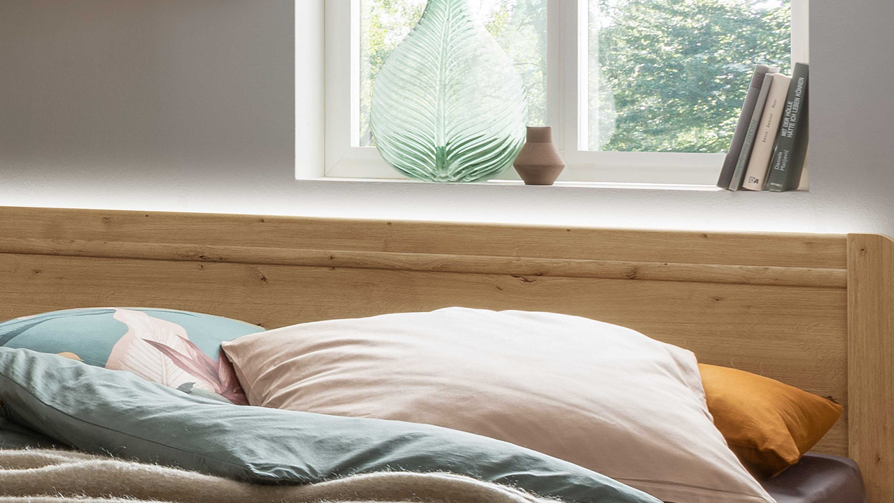 Holzkopfteil mit integrierter Beleuchtung hinter dem Bett mit Kissen in verschiedenen Farben