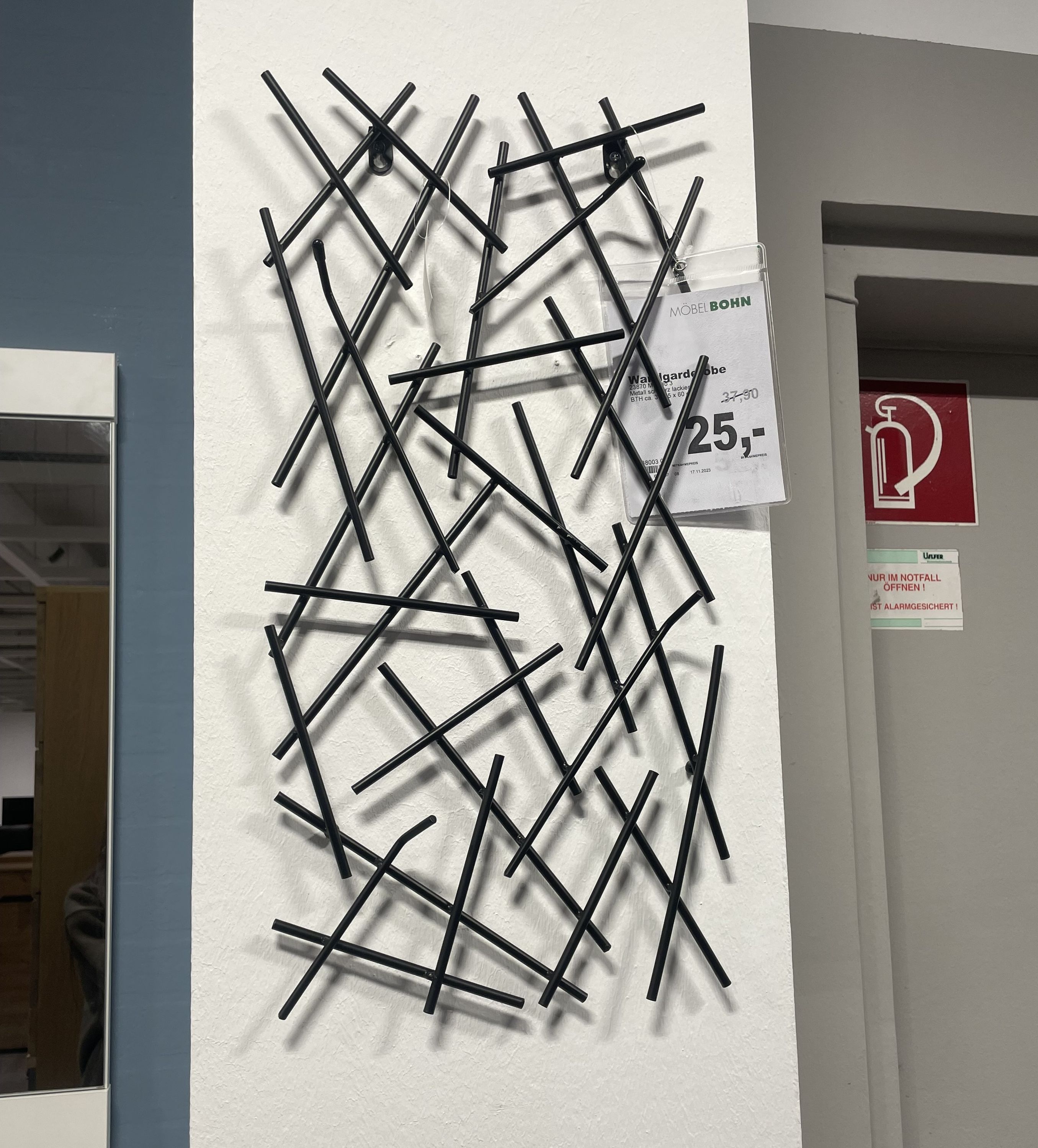 Schwarze Wandgarderobe mit überkreuzten Metallstäben an weißer Wand, Preisschild sichtbar.