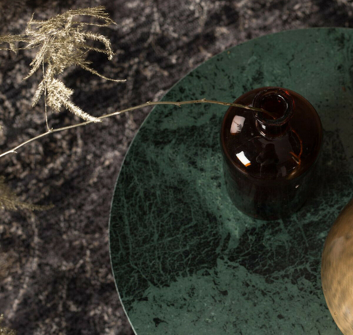Draufsicht auf grünen Marmortisch mit dunkler Glasvase und Trockenblume  vor einem strukturierten  dunklen Teppichboden