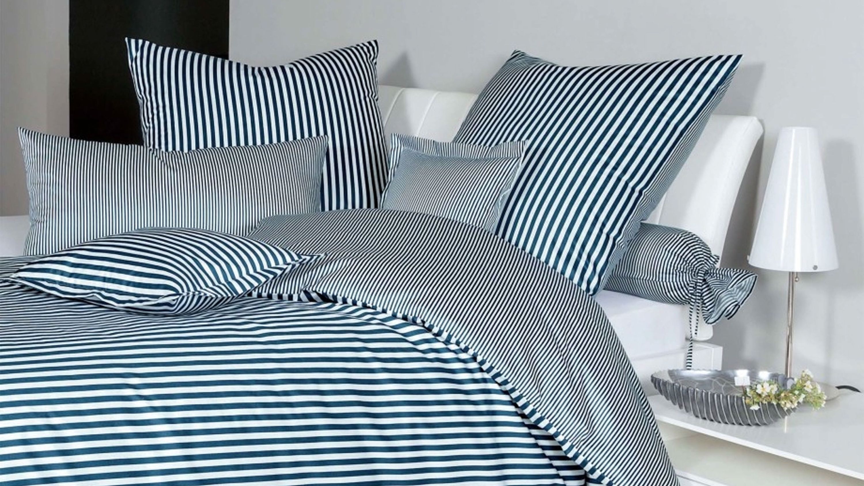 Bett mit gestreifter Bettwäsche in blau und weiß mit mehreren Kissen in verschiedenen Streifenmustern