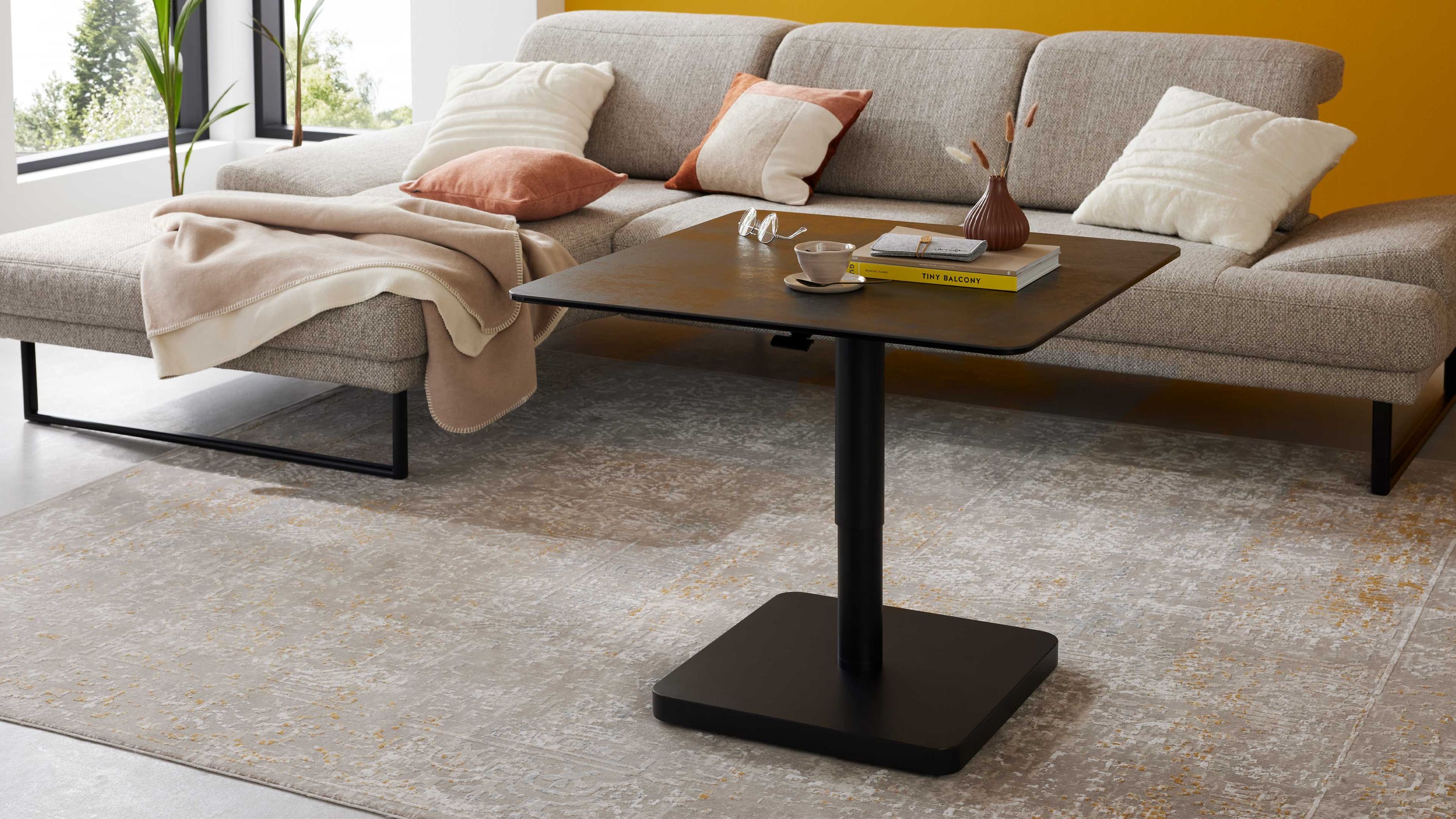 Quadratischer Couchtisch mit titanfarbener Oberfläche und schwarzem Metallgestell vor grauem Sofa