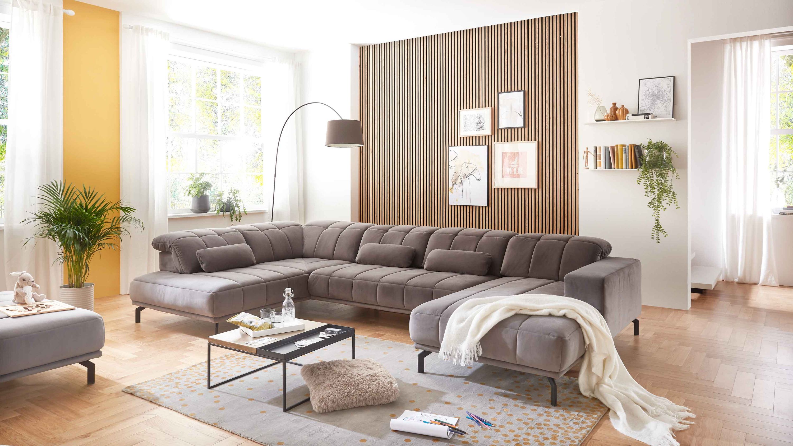 Große graue Wohnlandschaft mit schwarzer Metallstruktur in modernem Wohnzimmer mit Holzwand und großen Fenstern