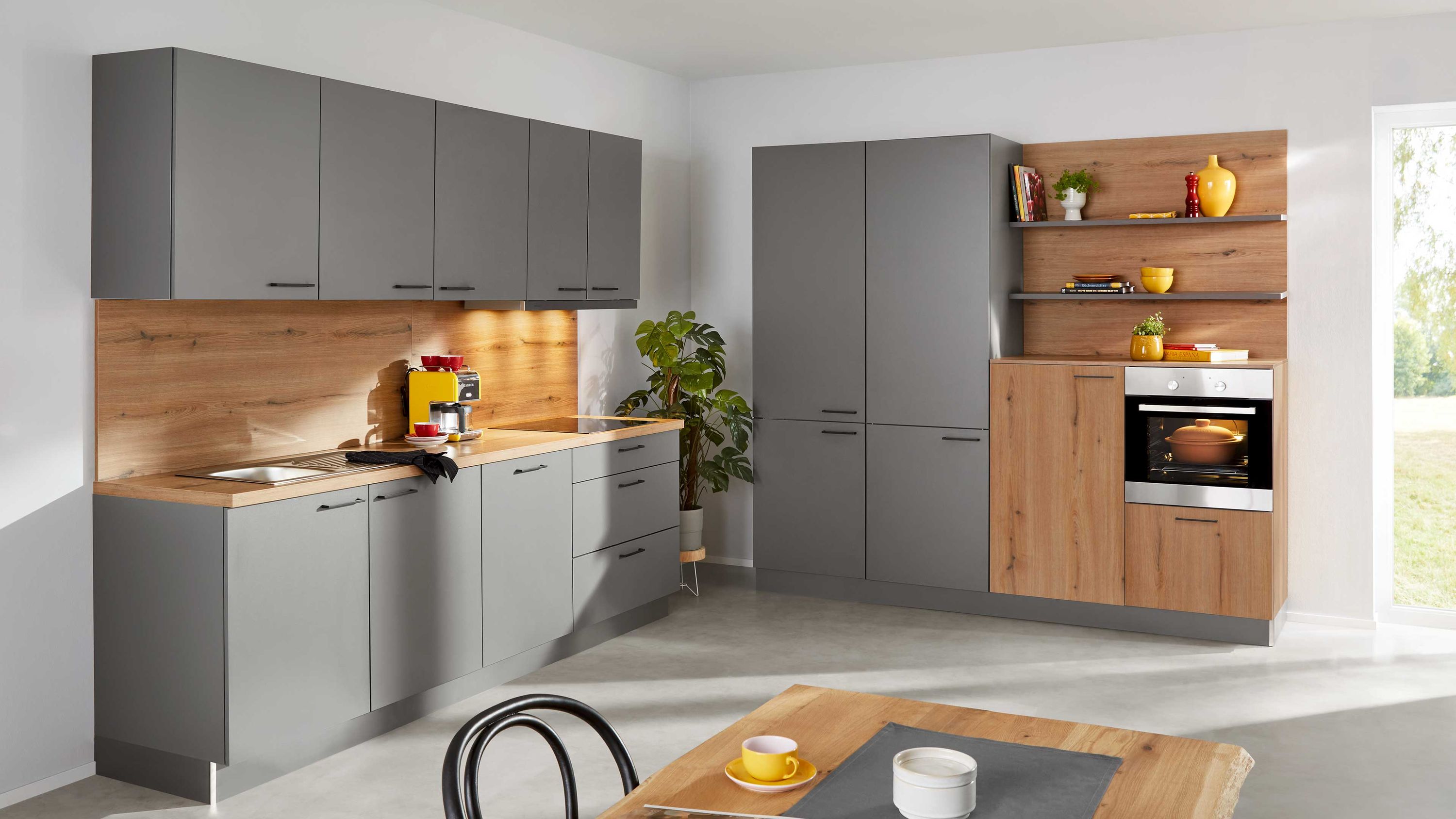 Graue Küche mit Holzdetails und gemütlichem Essbereich Graue Fronten Holzarbeitsplatte offene Regale Esstisch mit Geschirr Fensterlicht Einbauofen