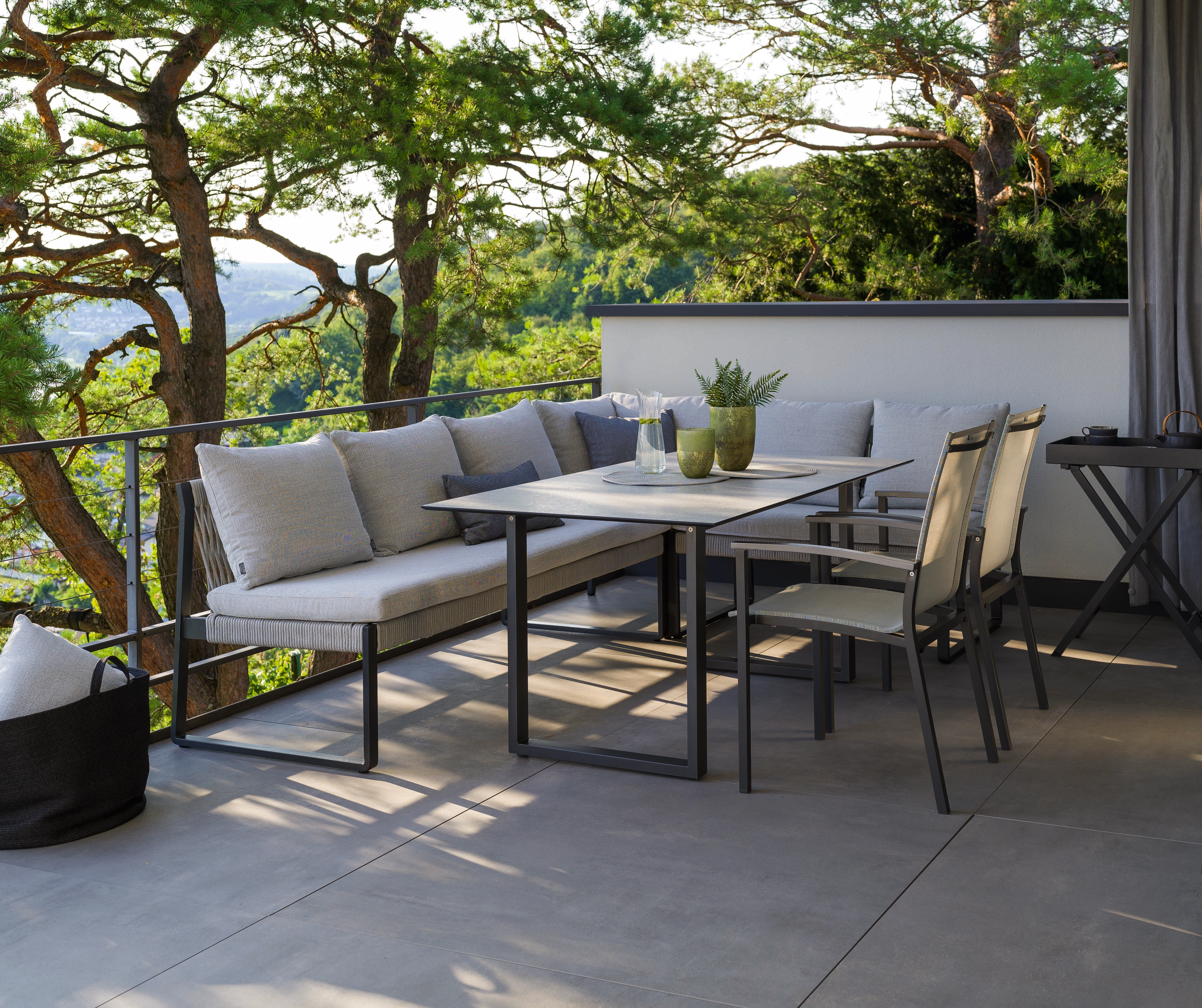 Moderne Loungemöbel mit Esstisch auf einer Terrasse, umgeben von Bäumen und Blick ins Grüne.
