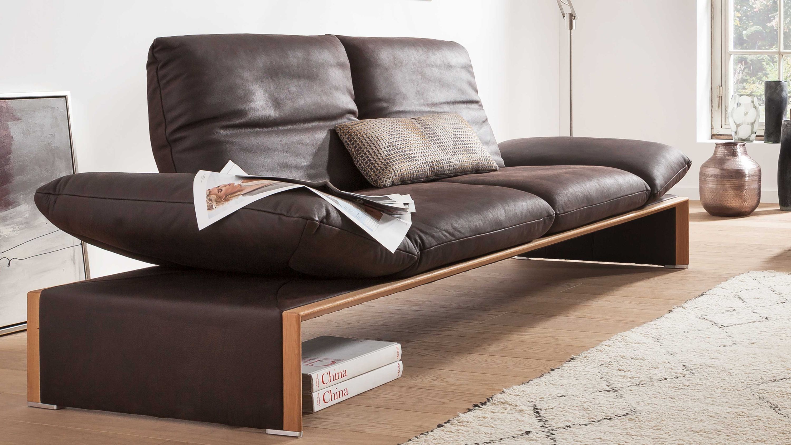 Zweisitziges Ledersofa mit Holzgestell Zweisitziges braunes Ledersofa mit breiten Armlehnen und Holzgestell in modernem Wohnzimmer