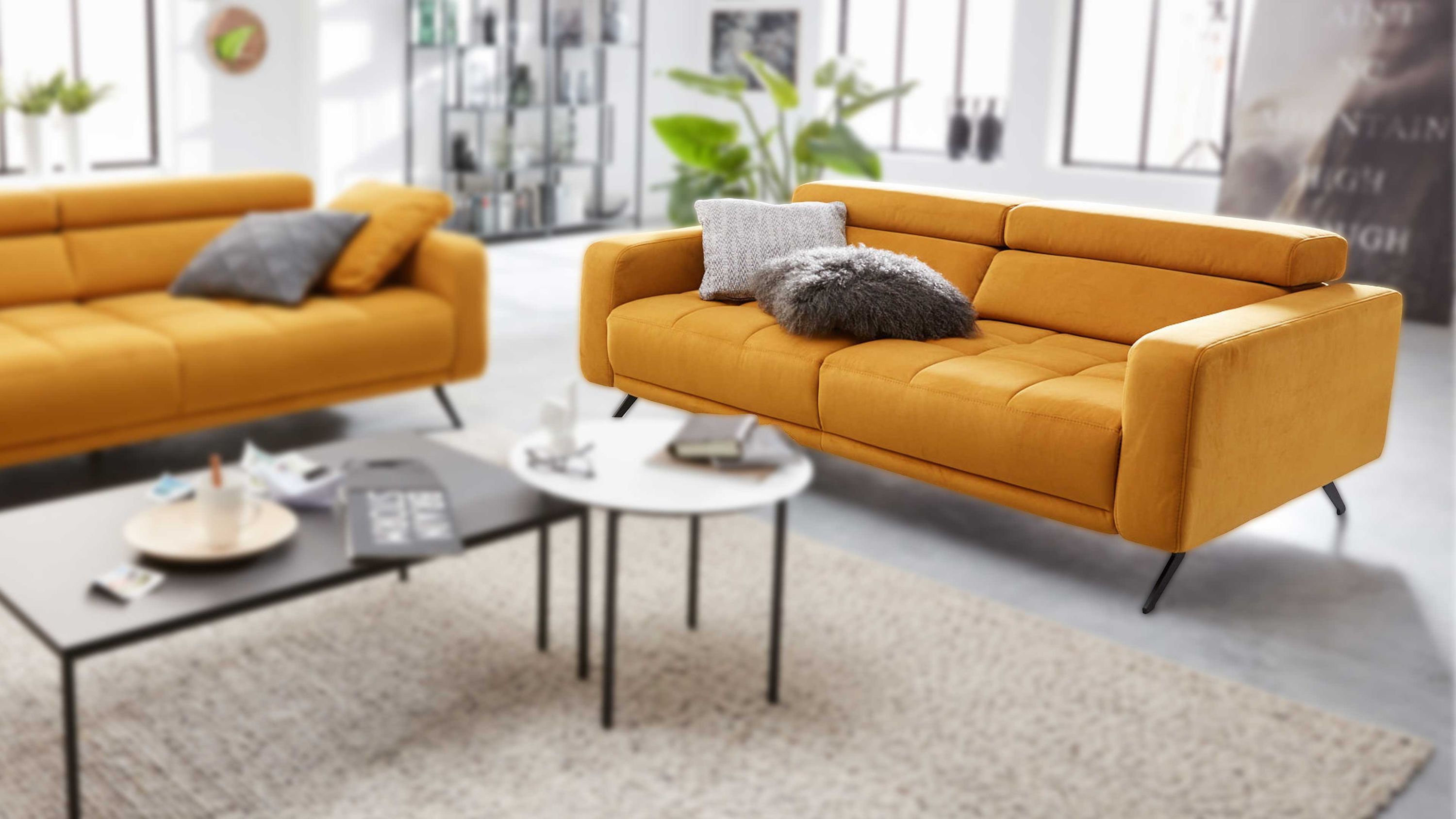 Zweisitziges Sofa in curryfarben mit gepolsterten Armlehnen und Rückenlehne dekoriert mit zwei Kissen