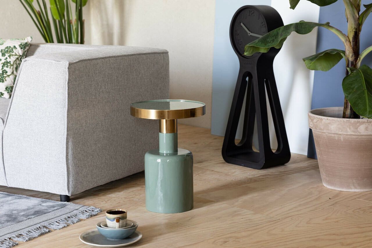 Kleiner runder Tisch mit grünem Sockel und goldener Platte dekorativ mit Skulptur Pflanze und Schale auf Holzfläche