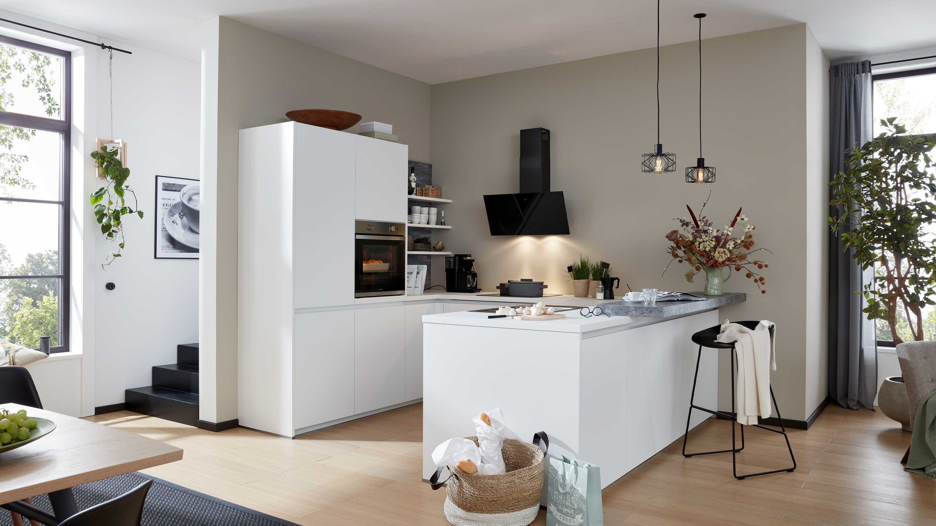 Helle Designküche mit Insellösung Kontrastelementen und wohnlicher Dekoration Weiße Küche mit Insel schwarzer Dunstabzugshaube Hängelampen Holzboden Fensterlicht Barhocker Dekopflanzen