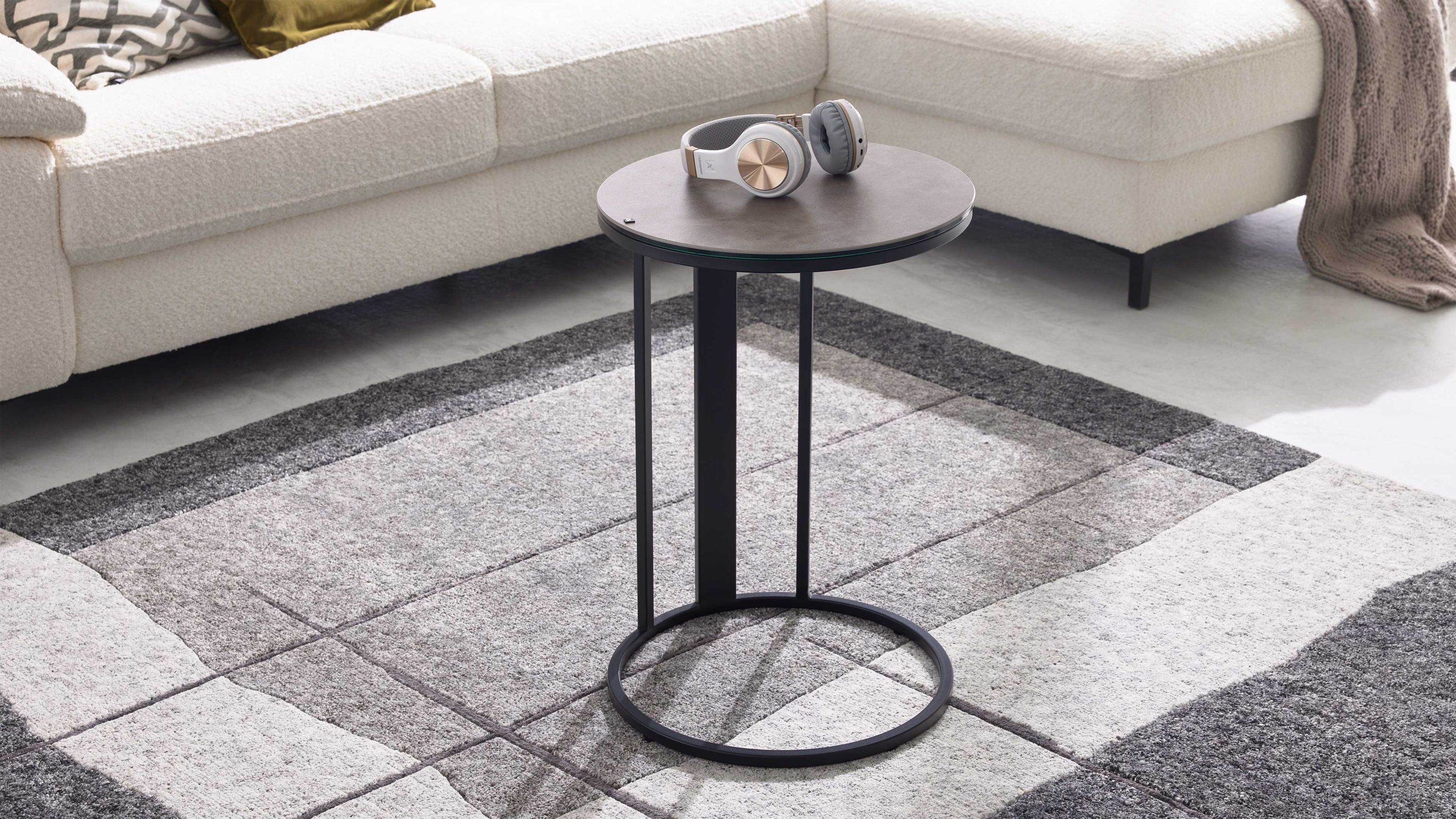 Runder Beistelltisch mit schwarzem Metallgestell und zementgrauer Oberfläche Runder Beistelltisch mit zementgrauer Oberfläche und schwarzem Metallgestell vor weißem Ecksofa auf grauem Teppich