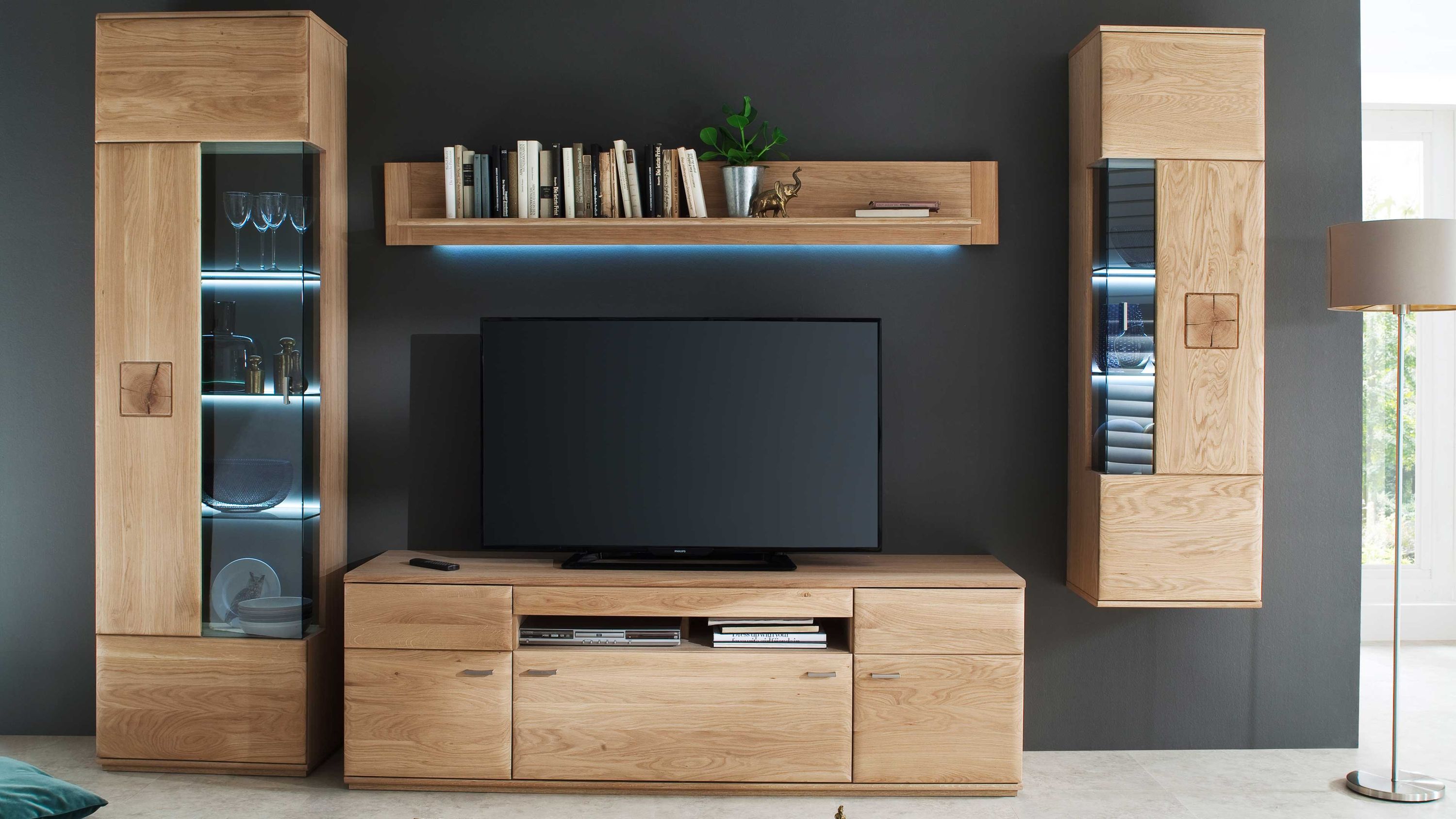 Vierteilige Wohnwand aus hellem Holz mit zwei Vitrinen einem TV-Board und einem Wandregal mit Büchern